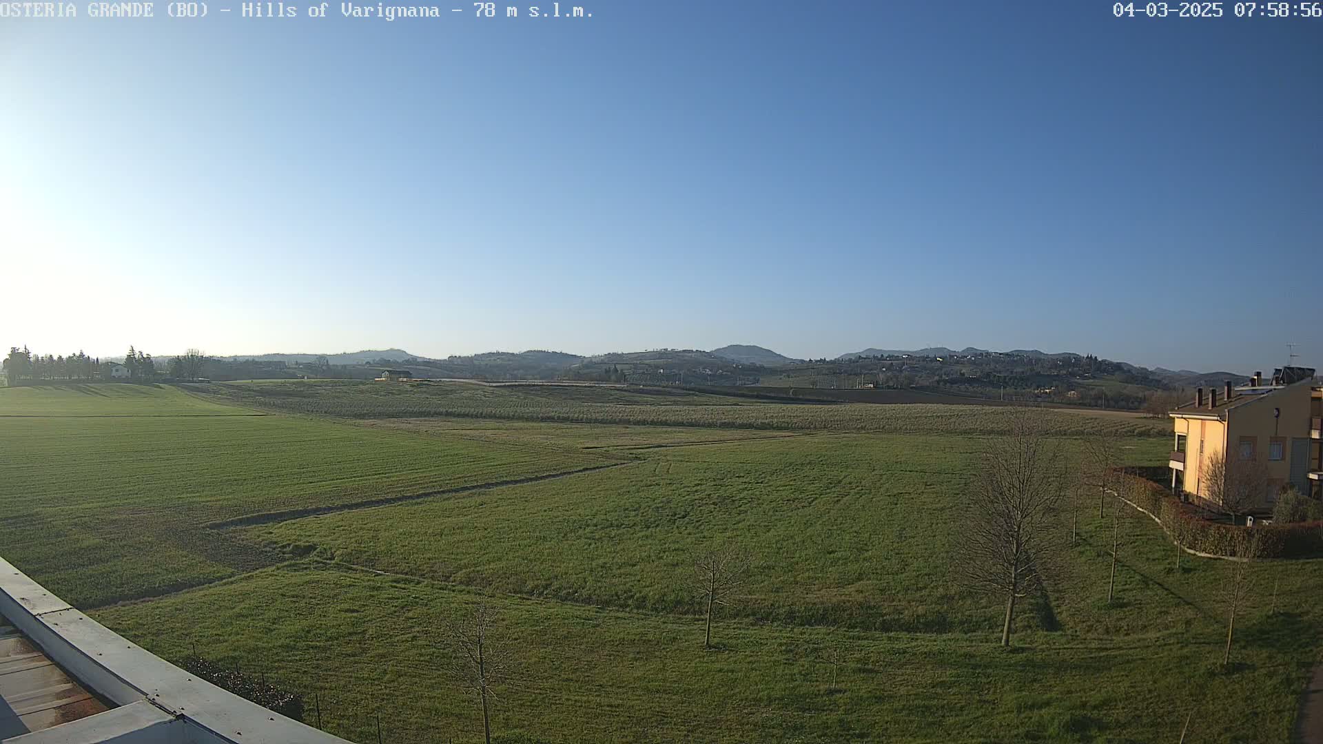 A wide, flat expanse of green farmland stretches to distant, low-lying hills under a clear blue sky.