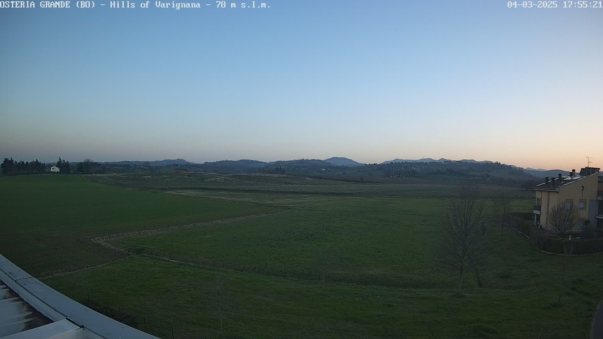 A wide, flat expanse of green fields stretches to a line of distant hills under a clear, twilight sky.