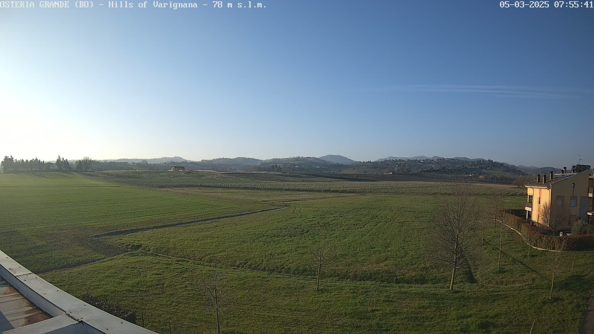 A wide, flat field of green grass stretches out to distant hills under a clear blue sky.