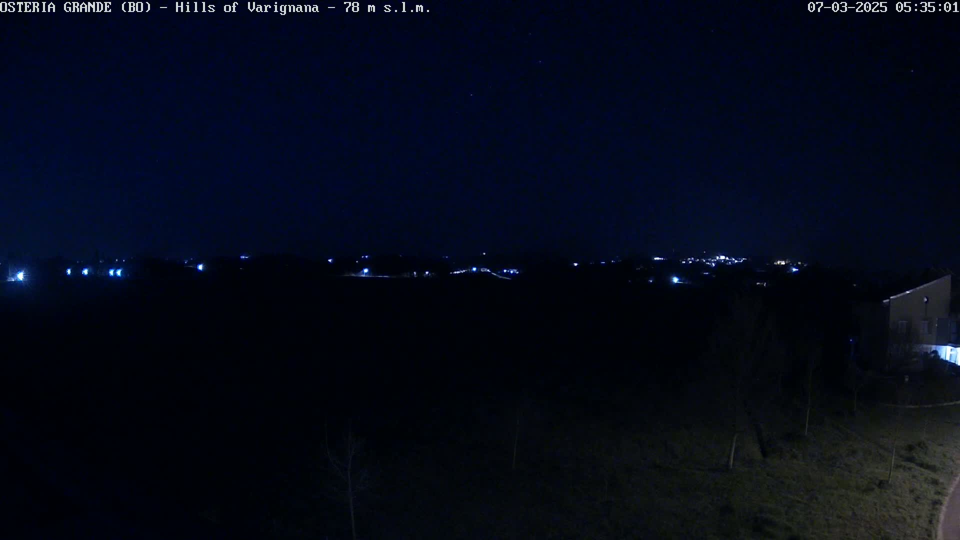 A dark, nighttime landscape shows a distant line of lights from a town or village under a clear, starlit sky.