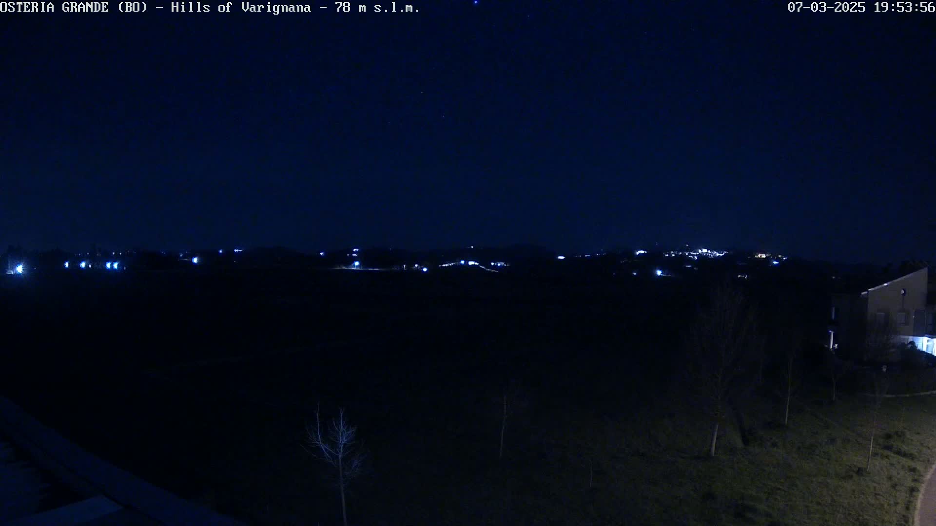 A nighttime view of sparsely lit hills and a few buildings under a clear, dark sky.