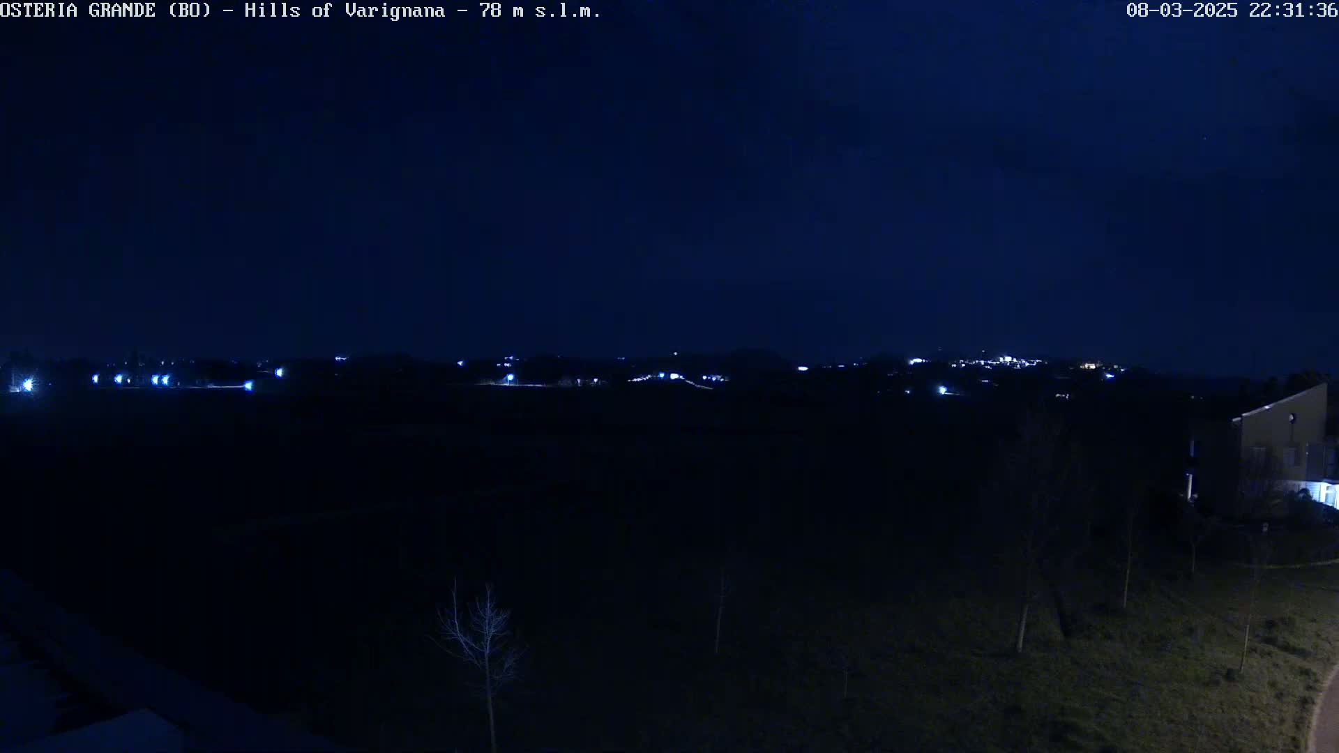 A nighttime view of dimly lit hills and a sparsely populated area under a dark, clear sky.