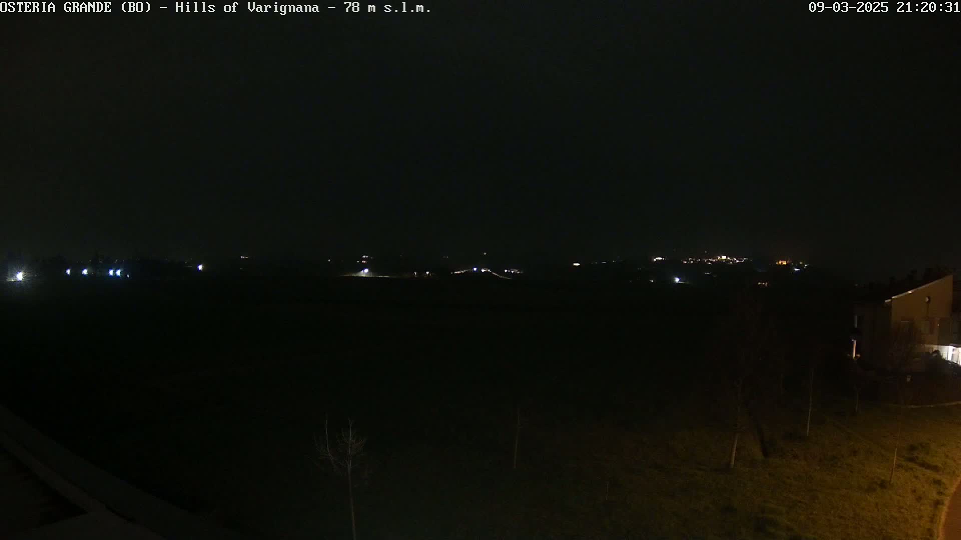 A nighttime view of dimly lit hills and a few distant buildings under a dark sky.