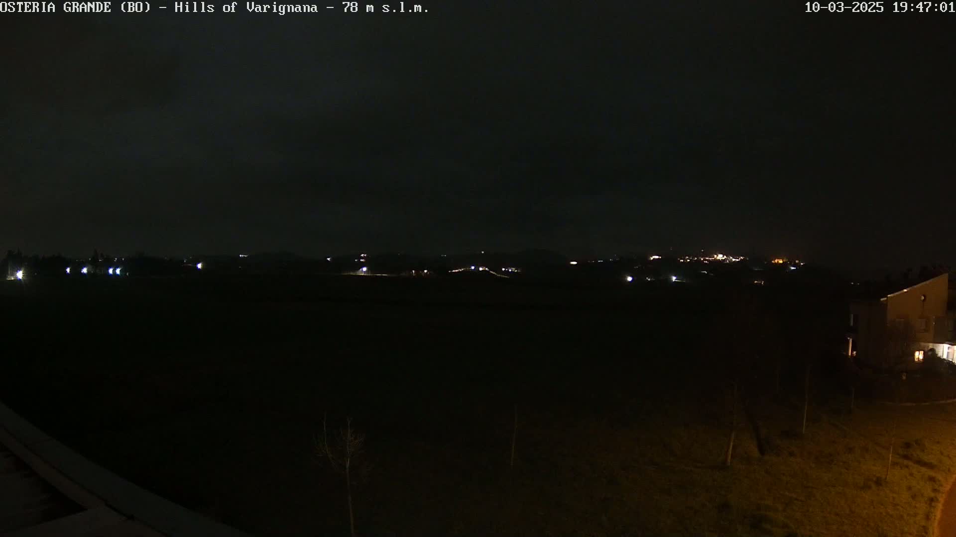 A nighttime view of dimly lit hills and a few buildings, under a dark sky.