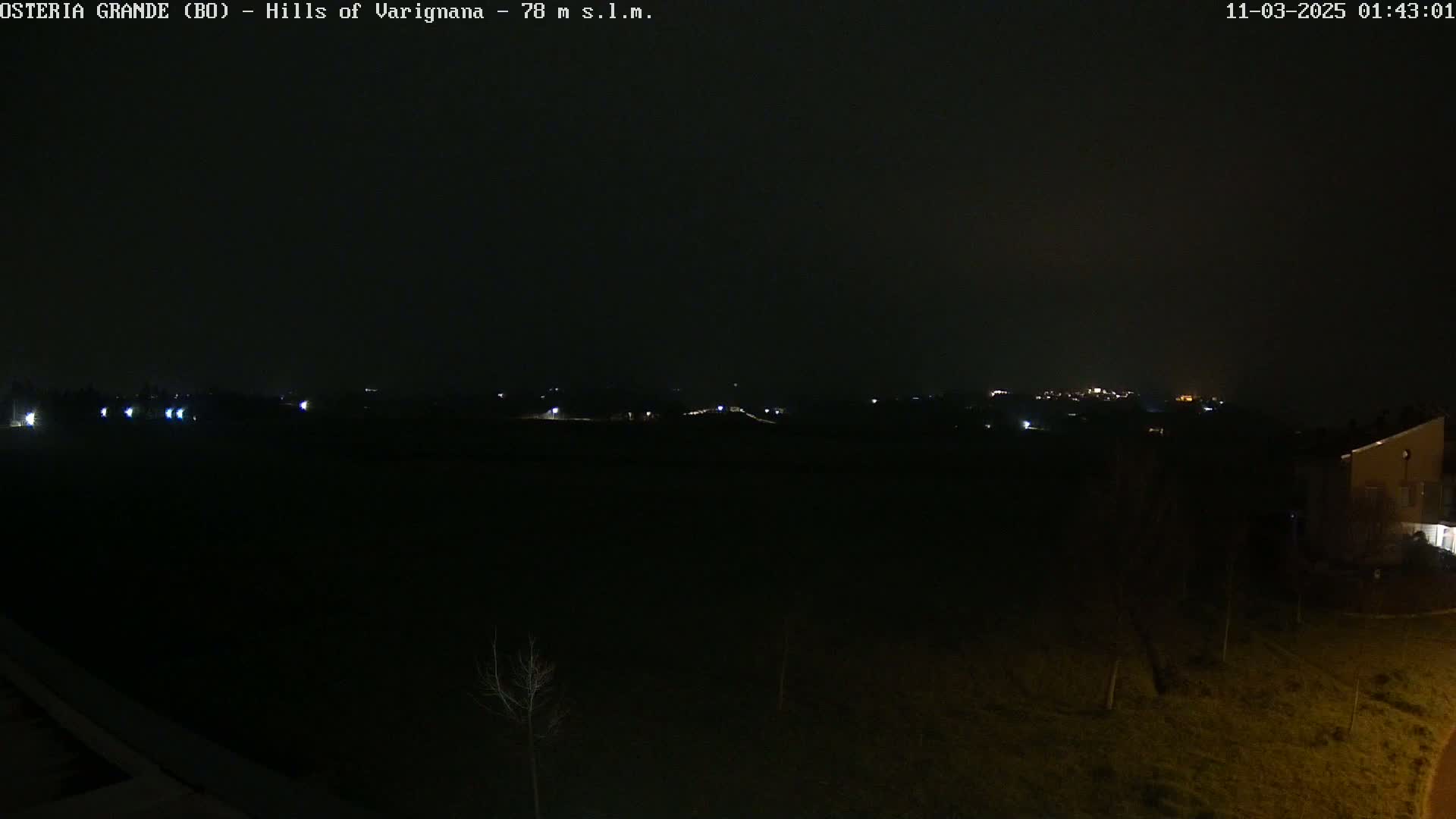A nighttime, dark view of a sparsely lit landscape with a few distant lights and a building on the right.