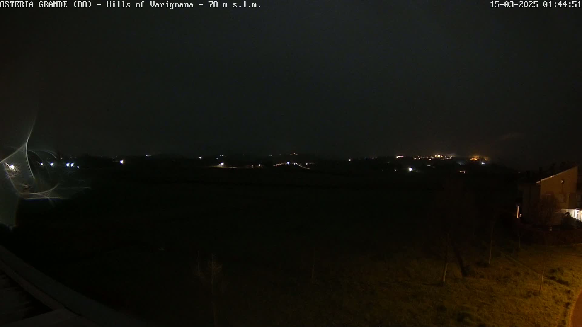 A nighttime, dark view of dimly lit hills in the distance under a cloudy sky.