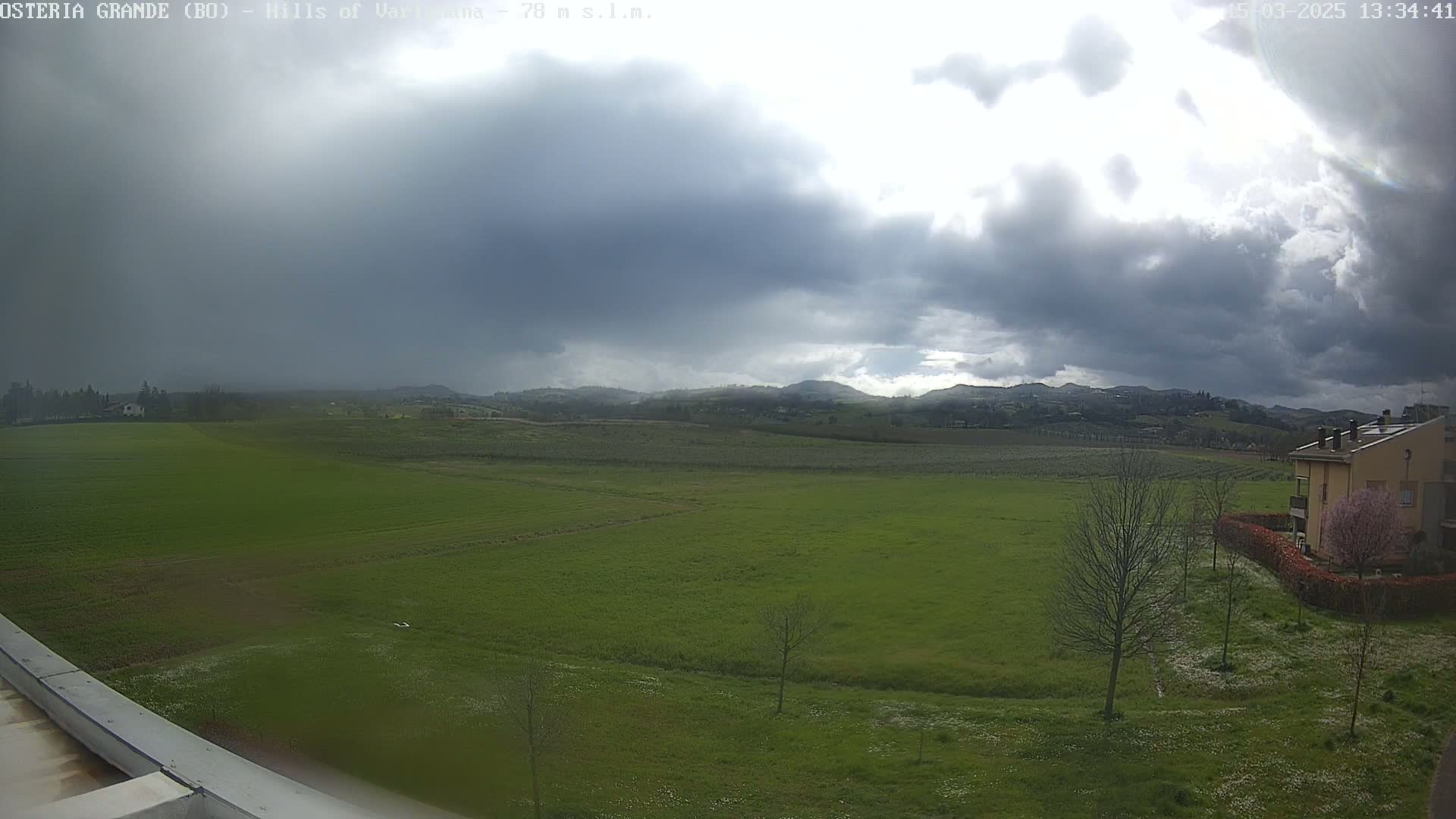 A wide, green field stretches to rolling hills under a mostly cloudy sky.