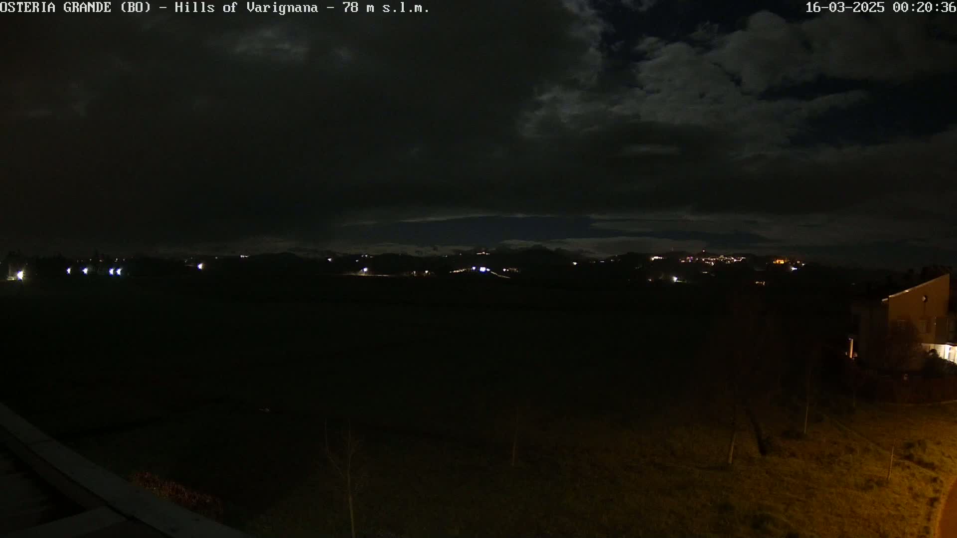 A nighttime view of dimly lit hills and a few buildings under a dark, cloudy sky.