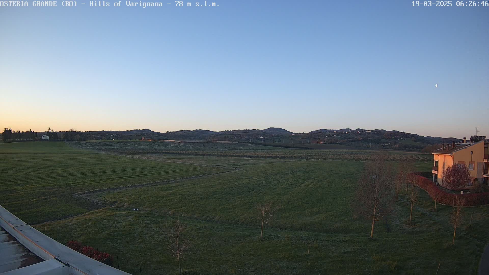 A wide, flat expanse of green farmland stretches to rolling hills under a clear, twilight sky.