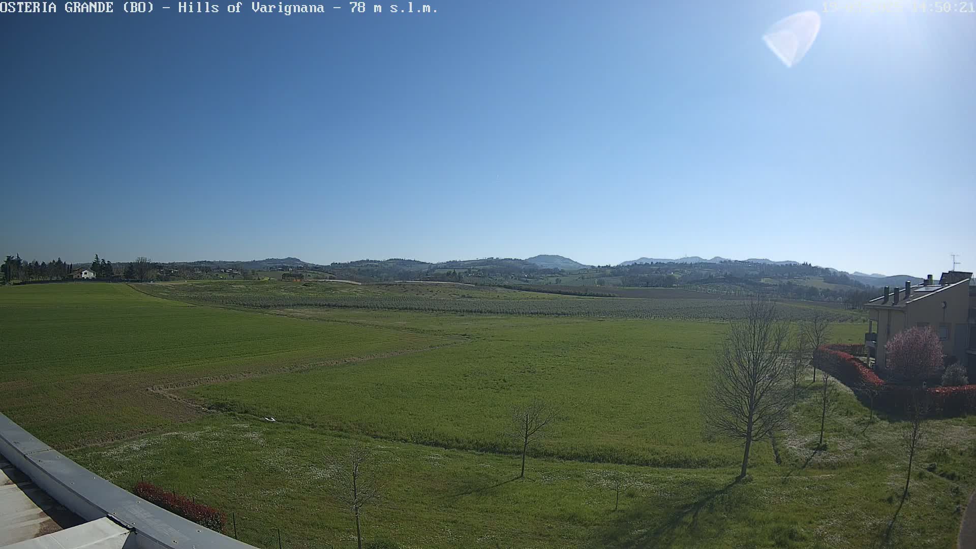 A vast expanse of green fields stretches towards a line of distant hills under a clear blue sky.