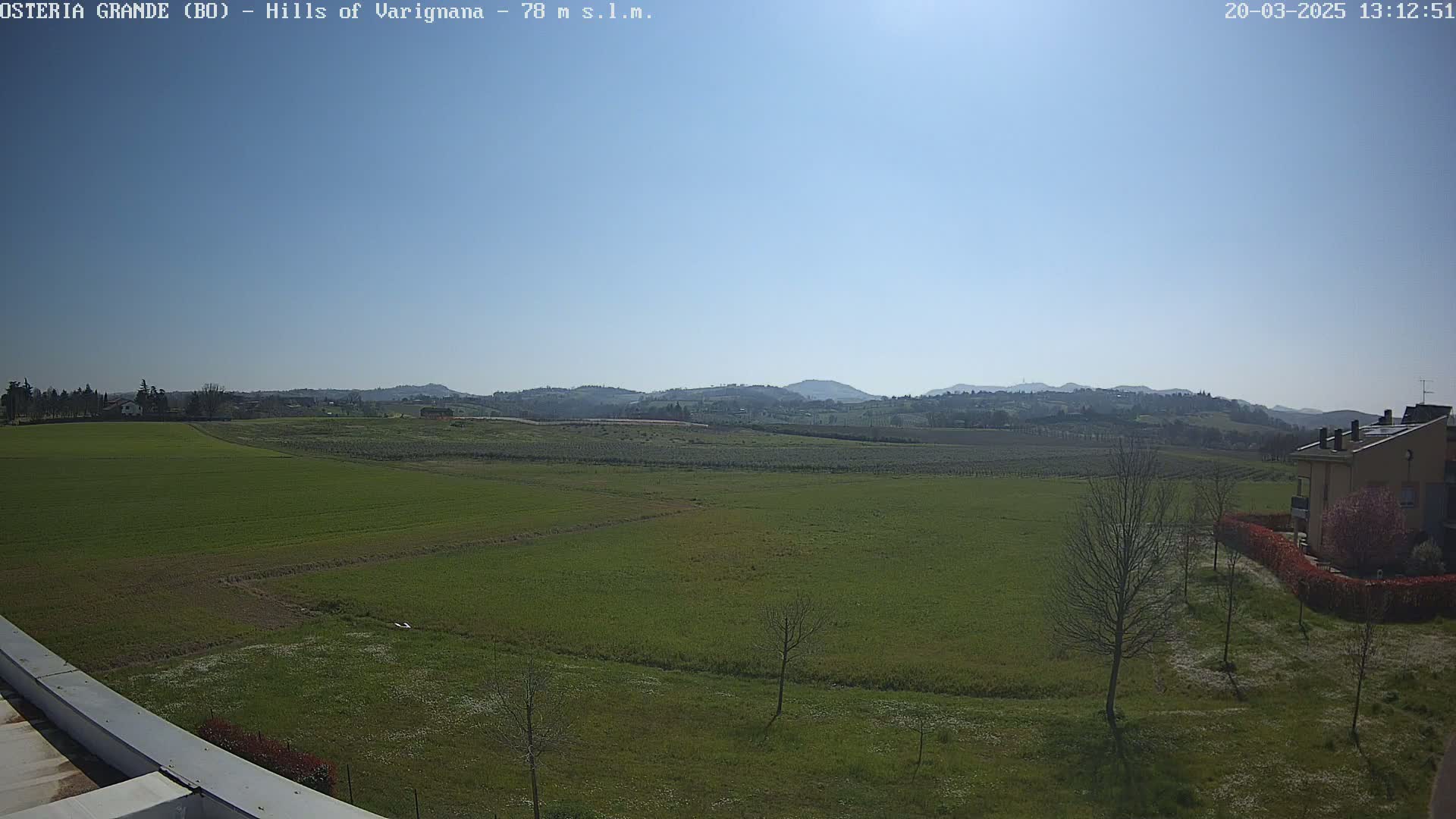 A sunny day reveals a vast expanse of green fields stretching towards distant, rolling hills under a clear blue sky.
