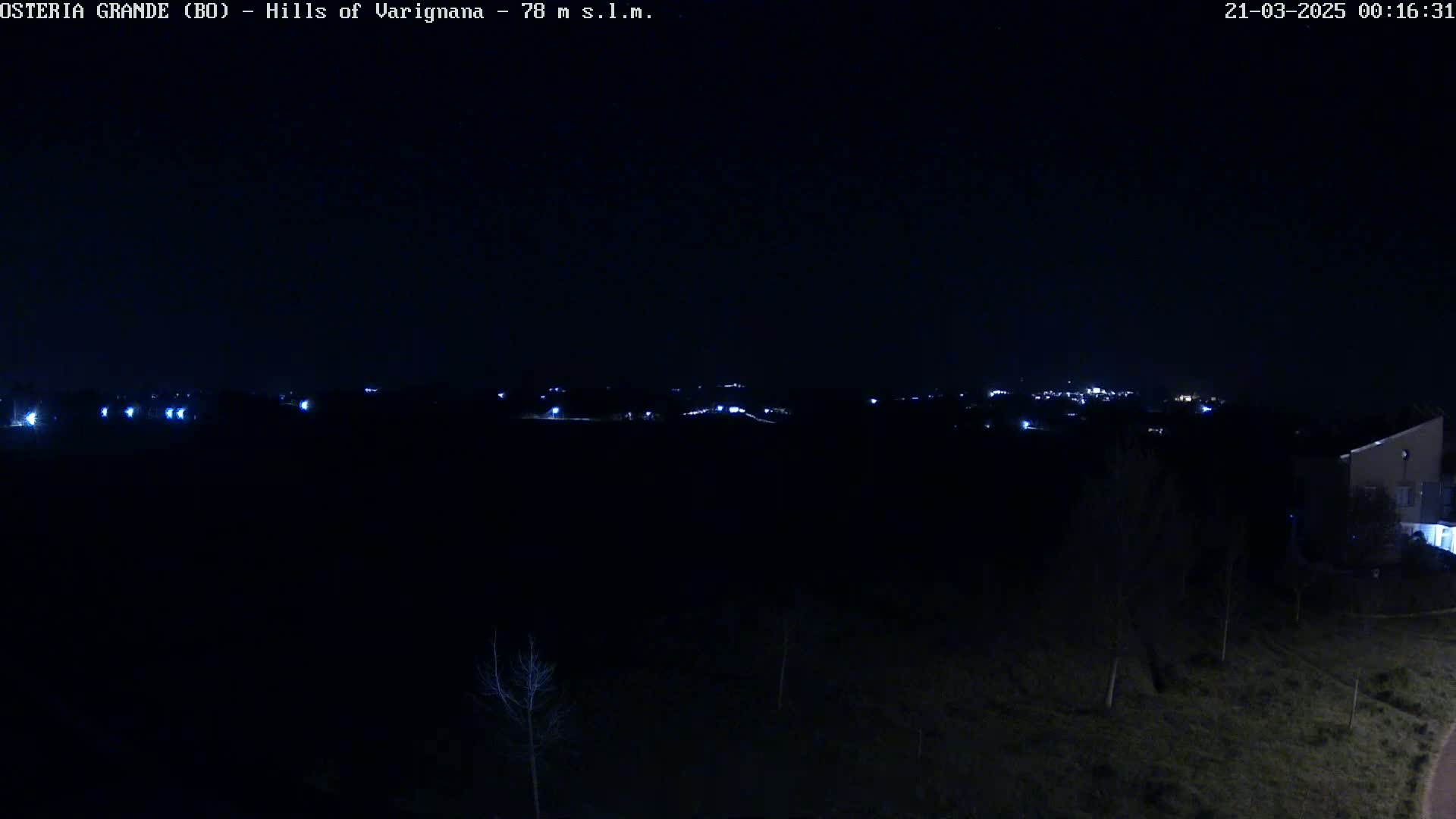 A nighttime view of a dimly lit landscape shows a distant town with scattered lights against a dark sky.