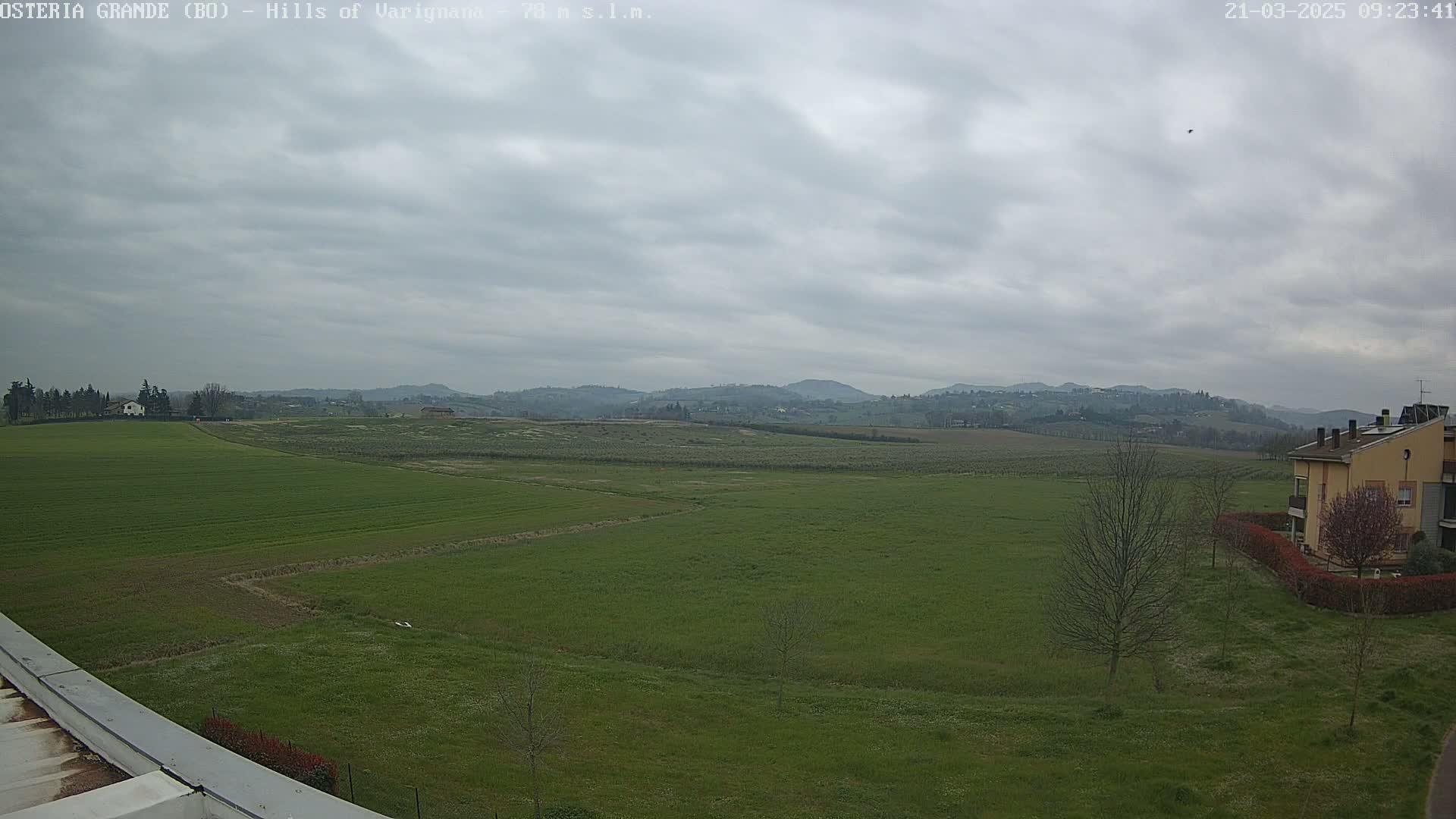 A wide, flat expanse of green fields stretches to rolling hills under a cloudy sky.