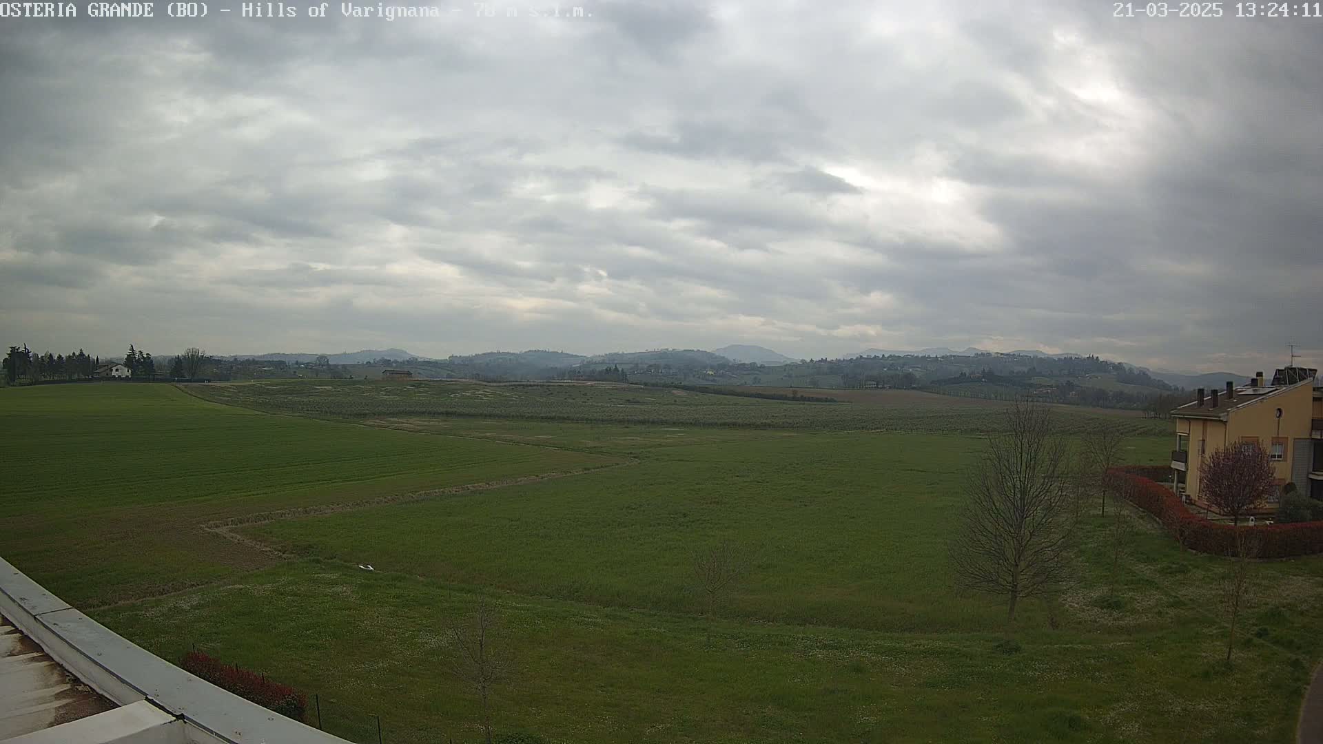 A sprawling green field stretches towards distant hills under a cloudy sky.