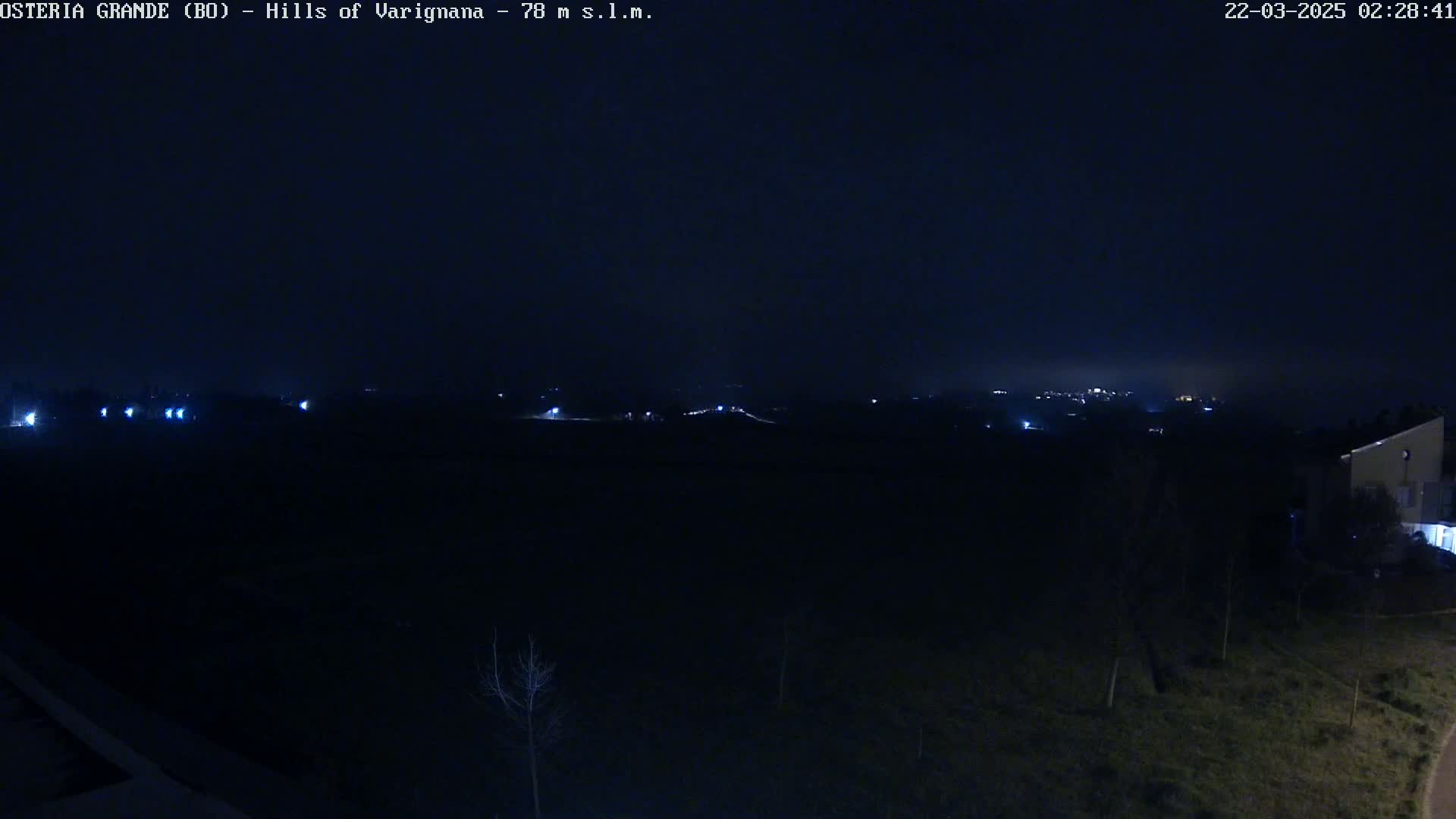 A dark, nighttime landscape showing distant lights in the hills under a clear, dark sky.