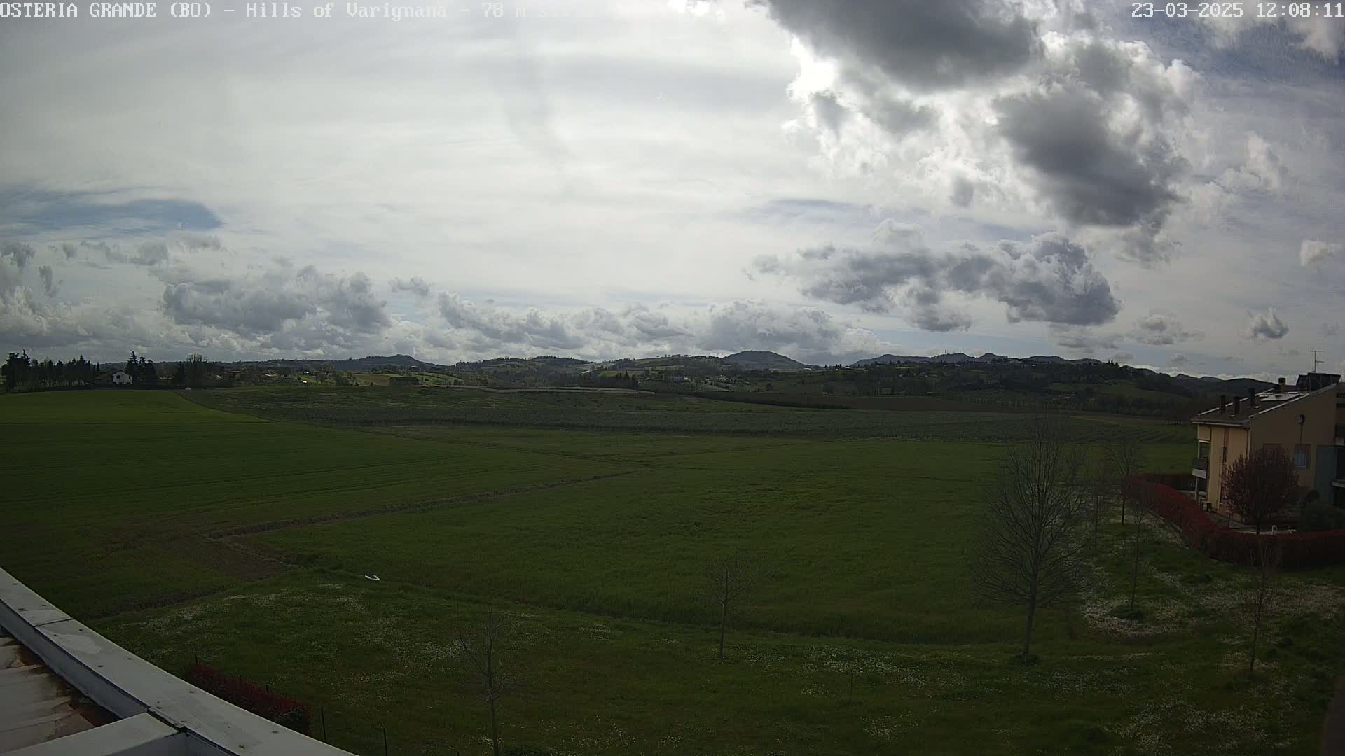 A sprawling green field stretches to rolling hills under a partly cloudy sky.