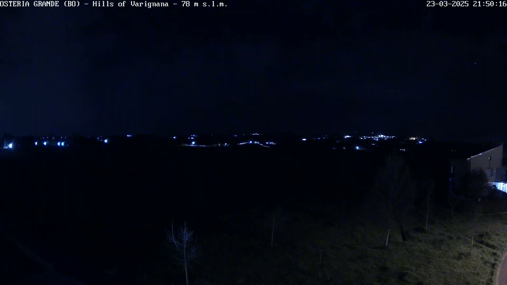 A nighttime view of a dark landscape with a few scattered lights in the distance and a building in the lower right corner.
