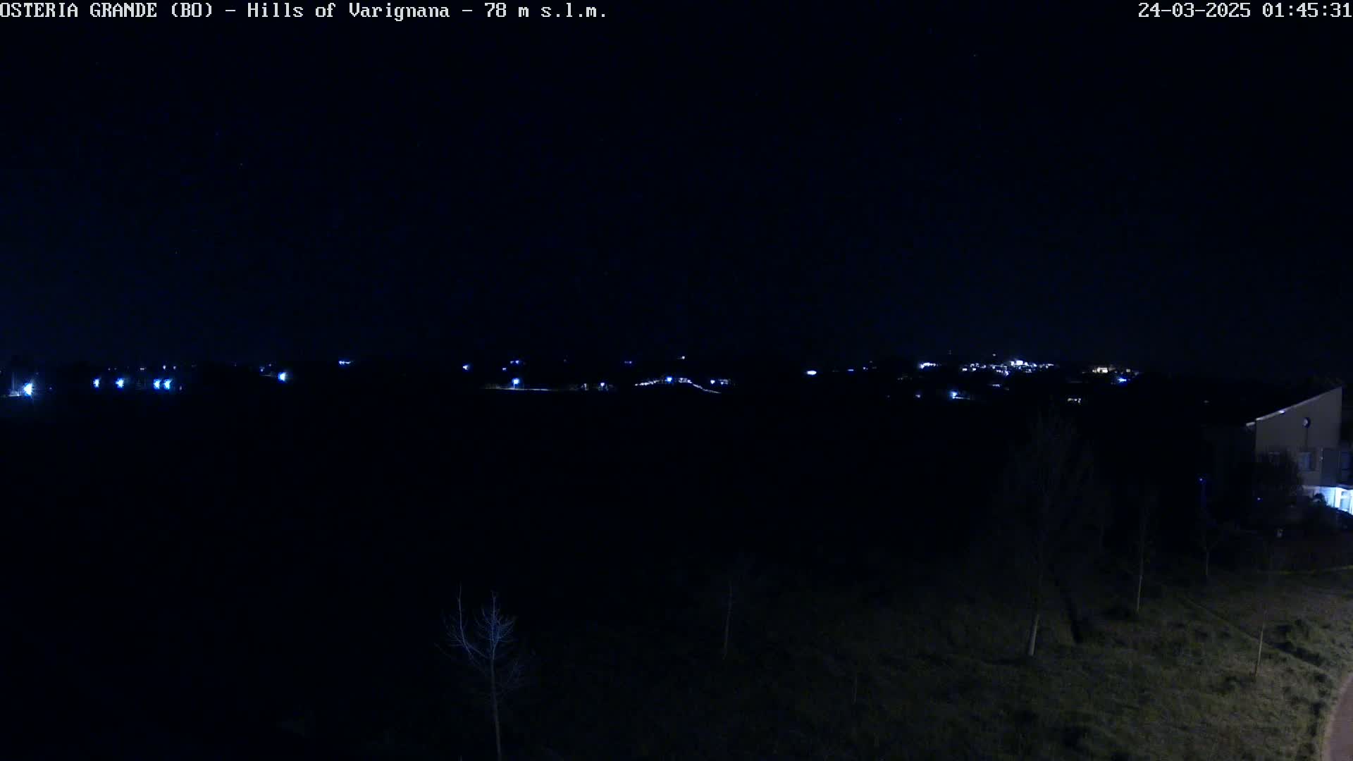 A nighttime view of a dark landscape with a distant line of lights, under a clear, dark sky.