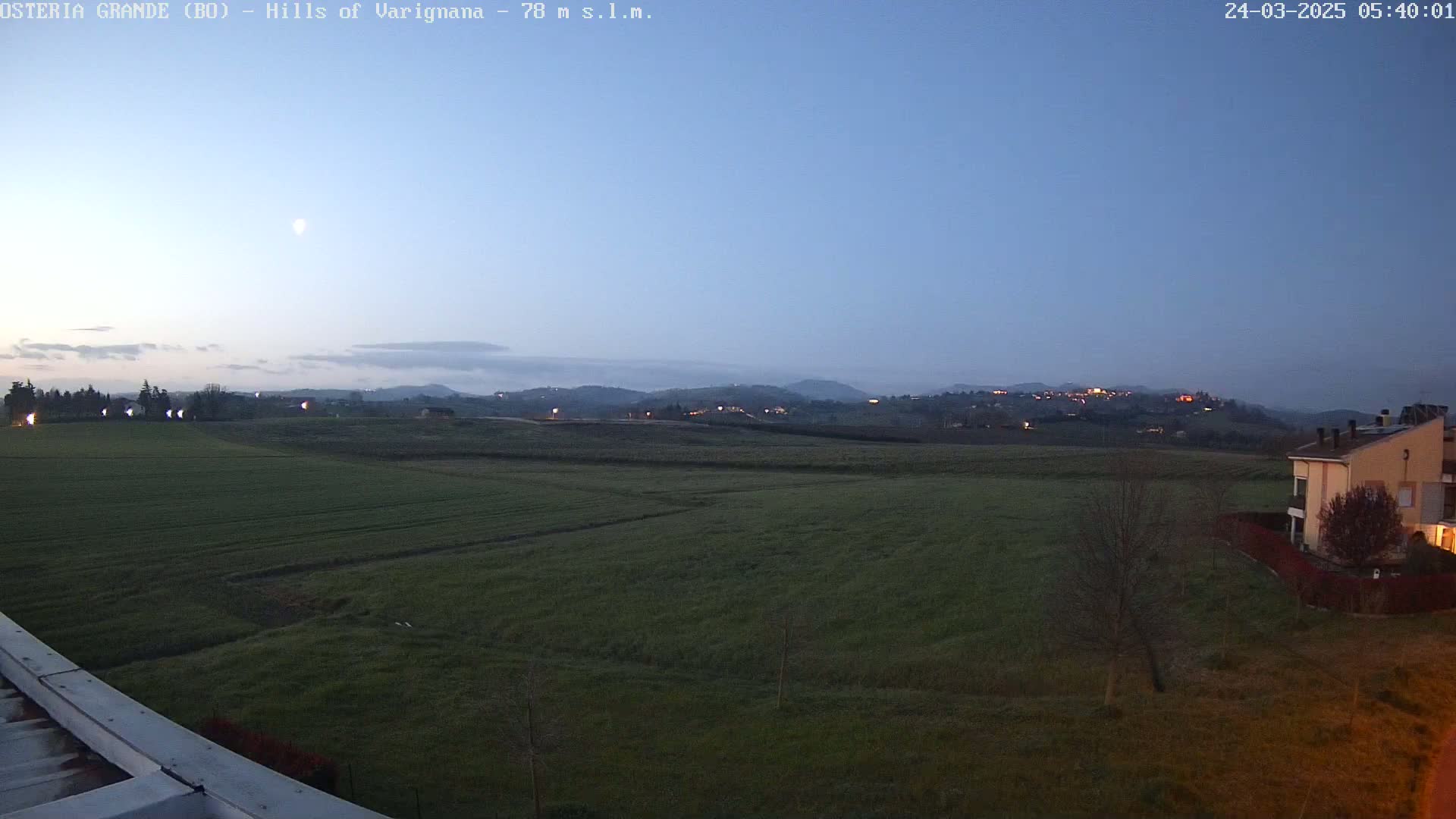 A twilight view shows a flat expanse of green farmland stretching to distant hills under a clear, dusky sky.