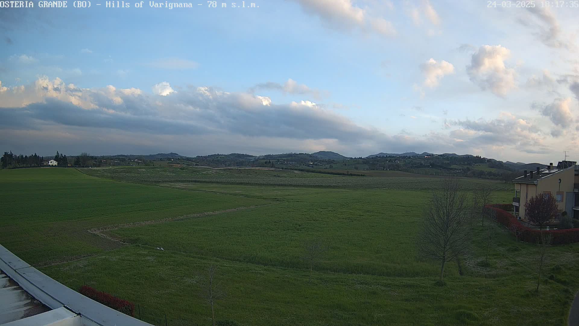 A wide, green field stretches to rolling hills under a partly cloudy sky.