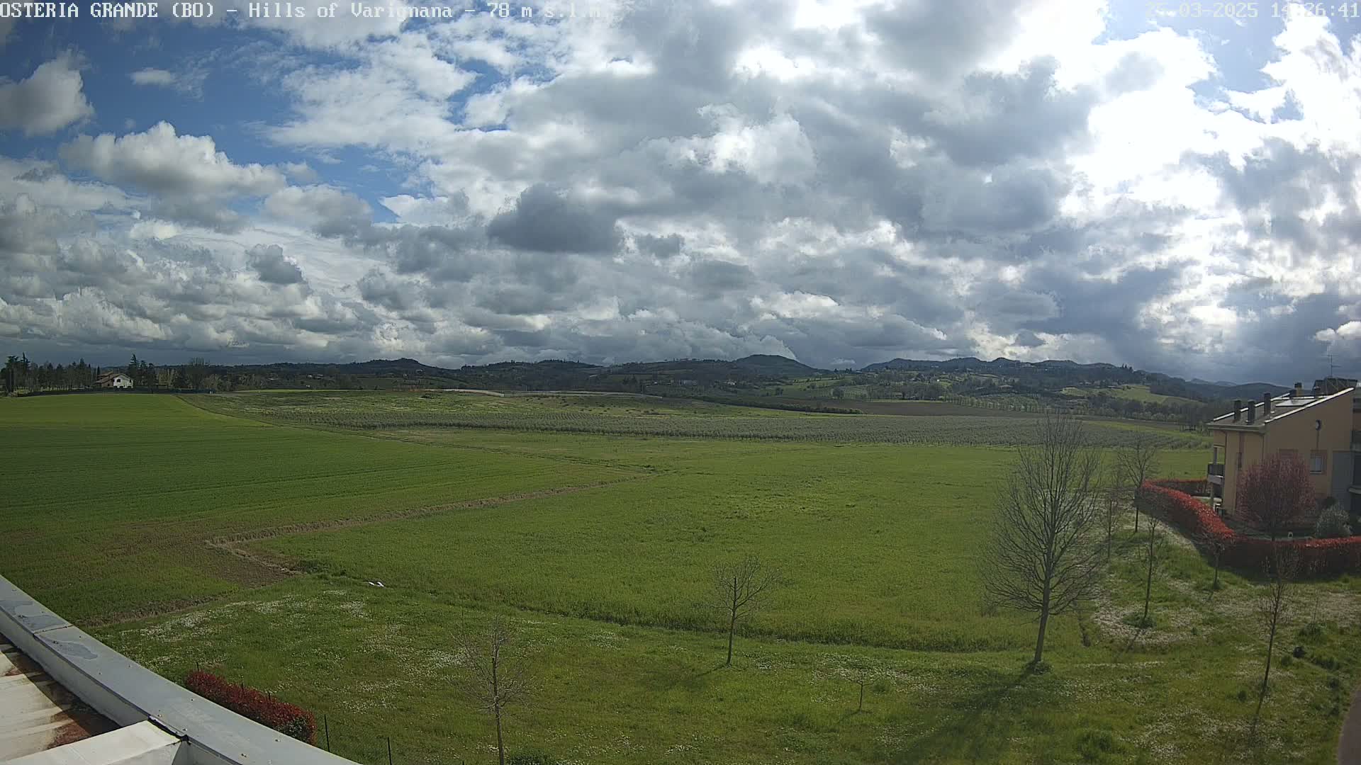 A partly sunny day reveals a vast expanse of green fields and distant rolling hills under a mostly cloudy sky.