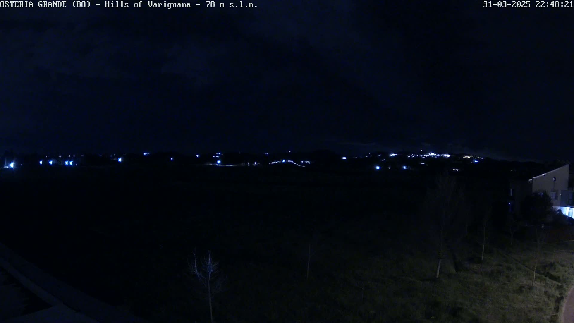 A nighttime view of dimly lit hills and a few scattered lights in the distance, under a dark sky.