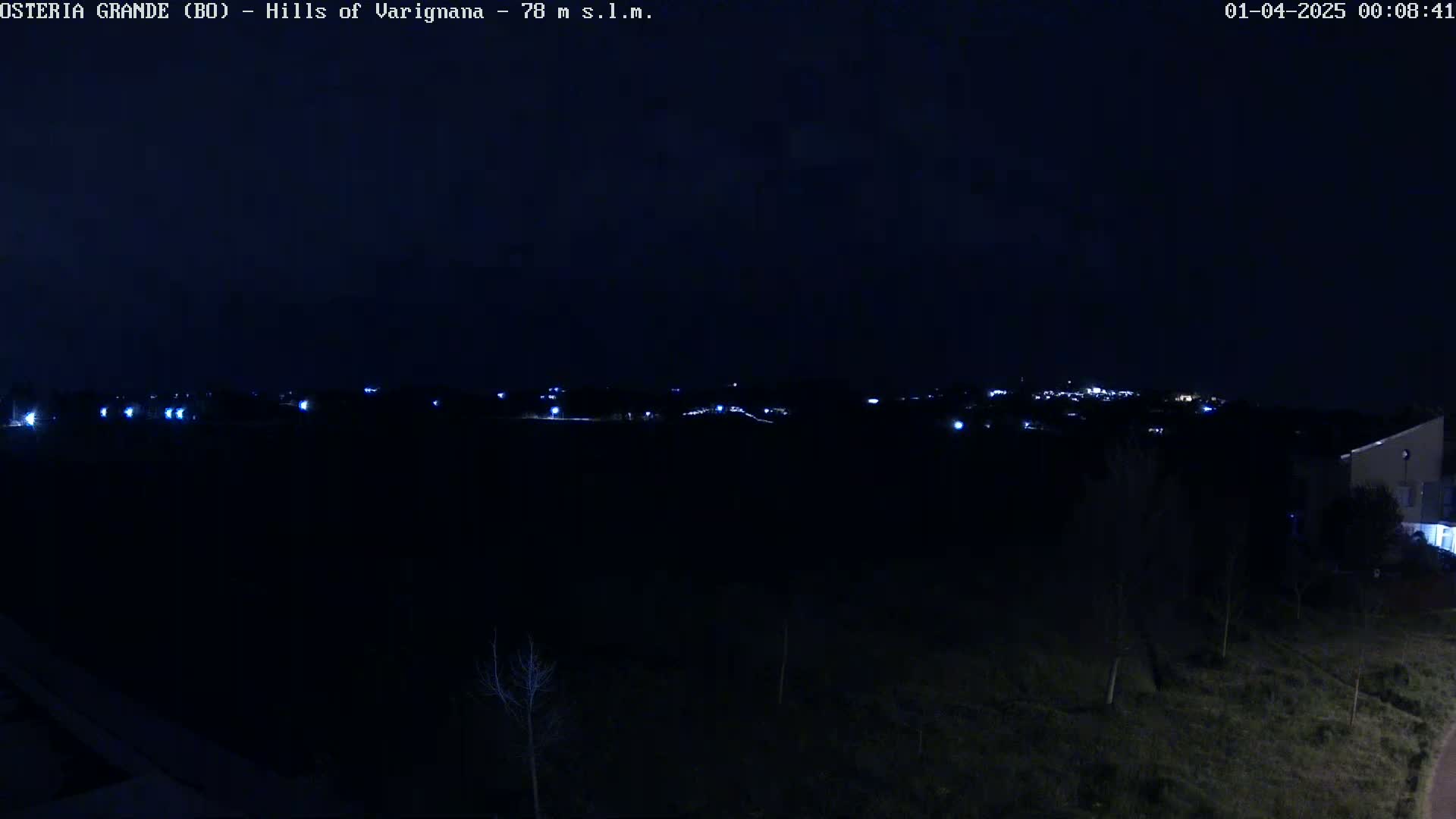 A nighttime view of dimly lit hills and a small town in the distance, under a dark sky.