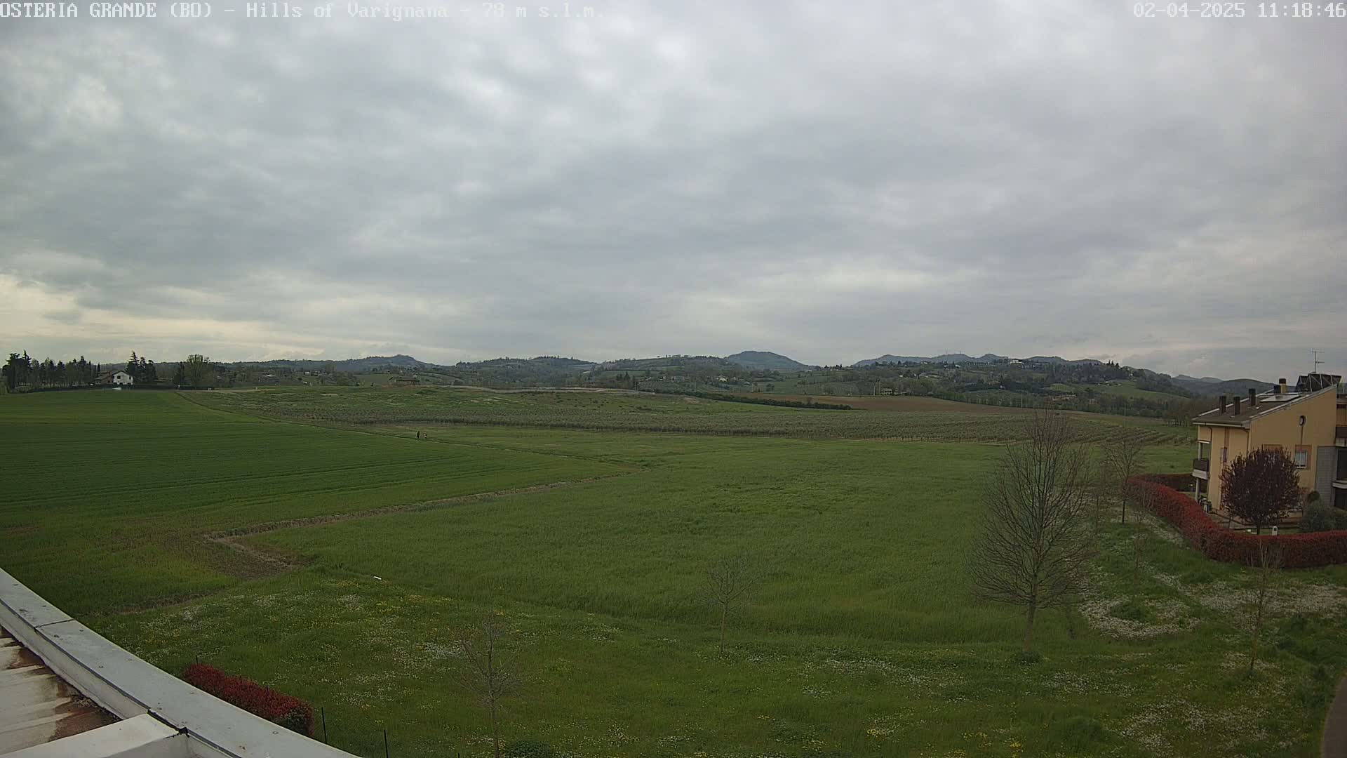 A wide, flat expanse of green fields stretches towards distant, rolling hills under a cloudy sky.