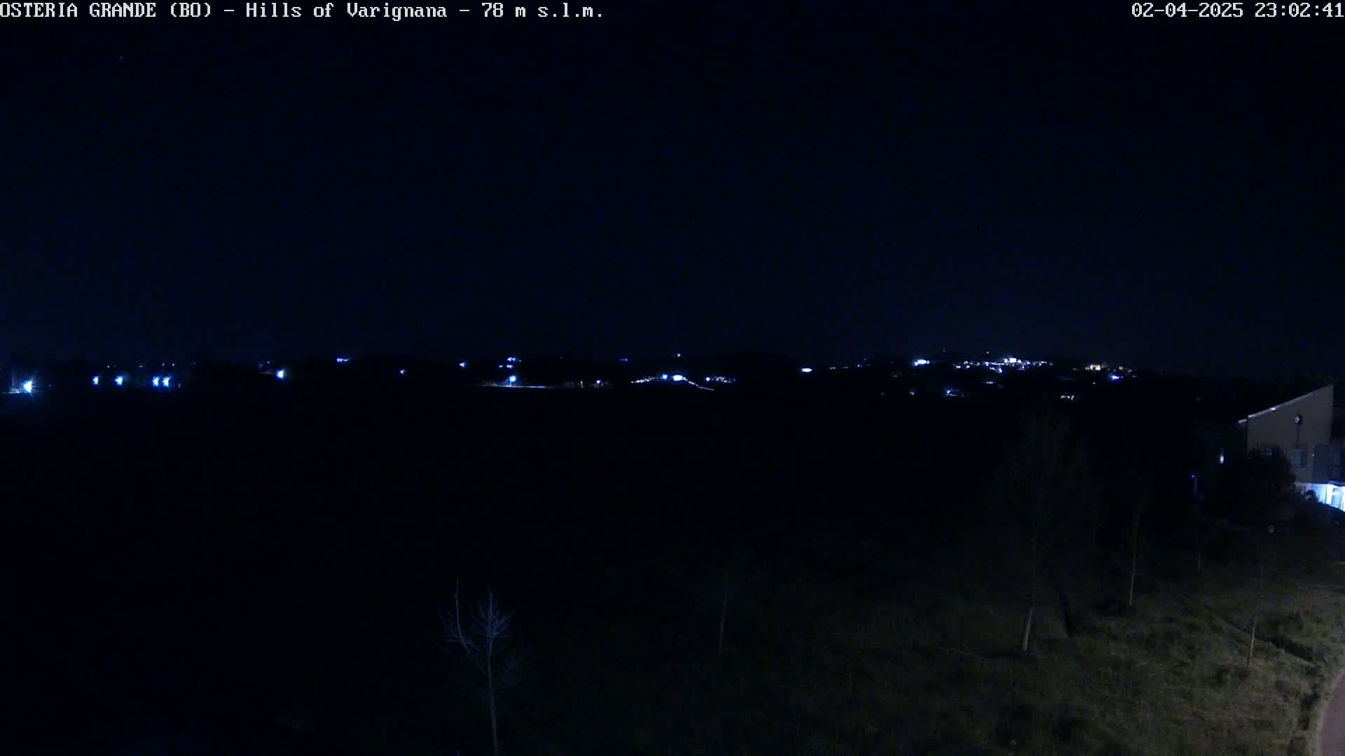 A nighttime, long-range view shows a dark landscape with a distant cluster of lights, likely a town, under a clear, dark sky.