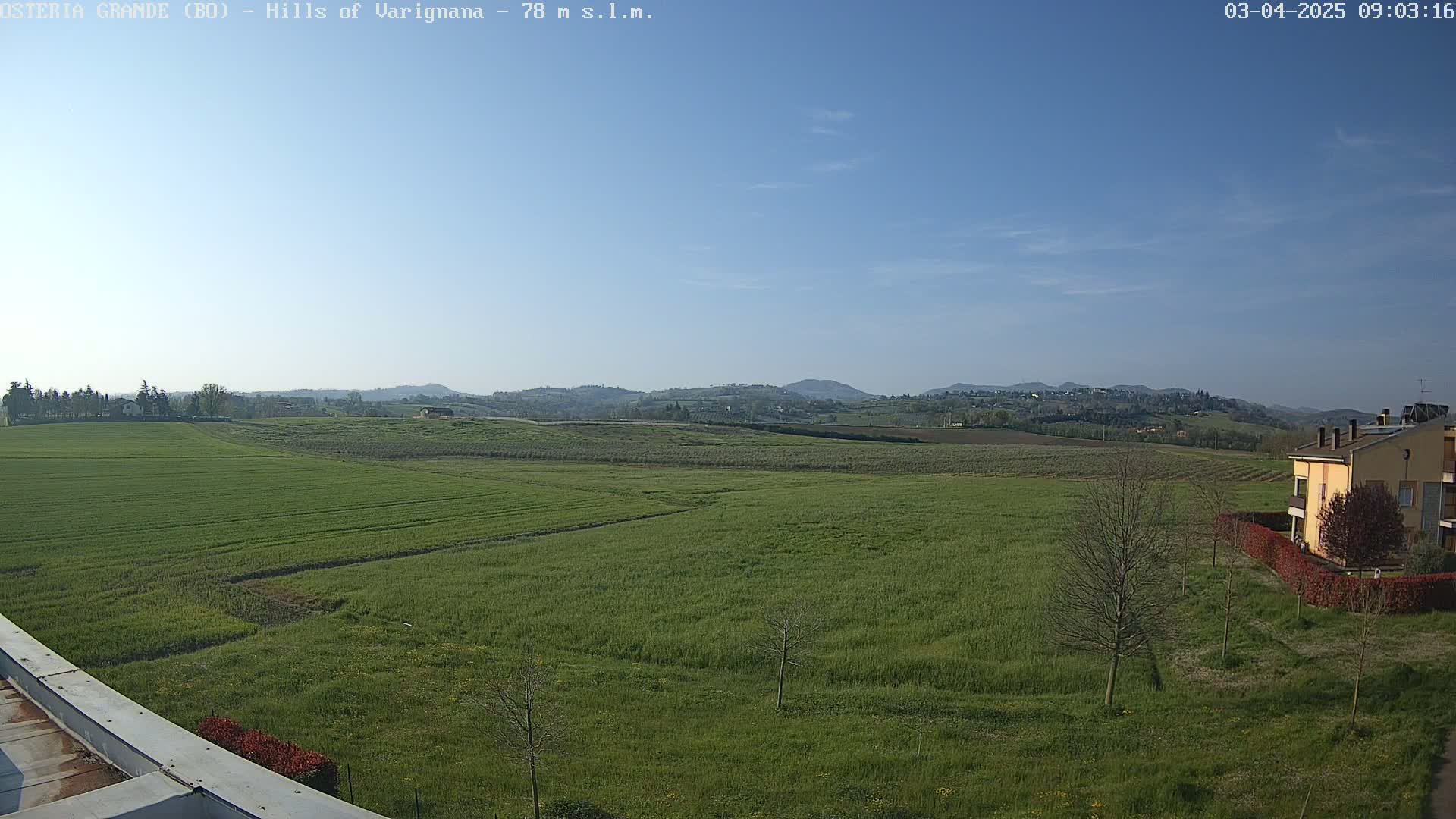 A wide expanse of bright green farmland stretches to rolling hills under a clear blue sky.