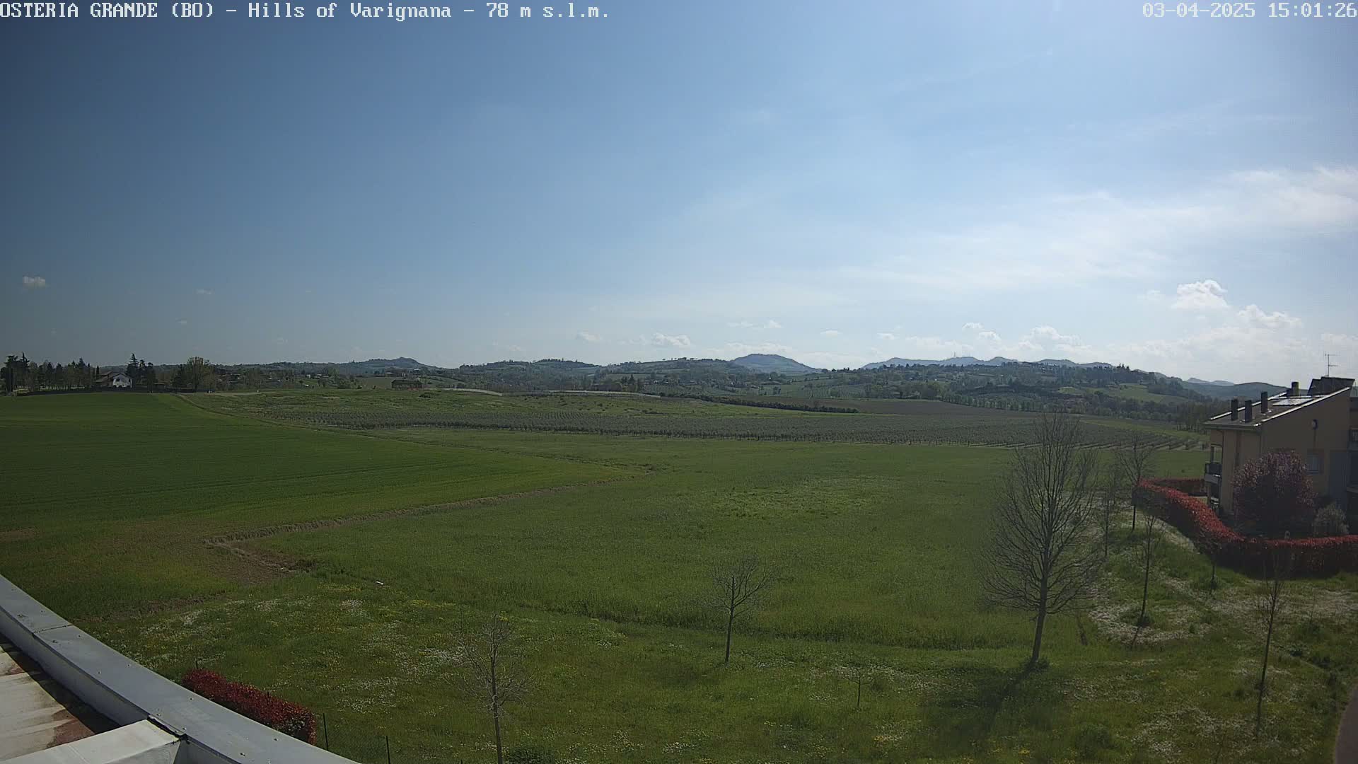 A mostly sunny day reveals a sprawling landscape of green fields and distant hills, with a few buildings visible in the foreground.