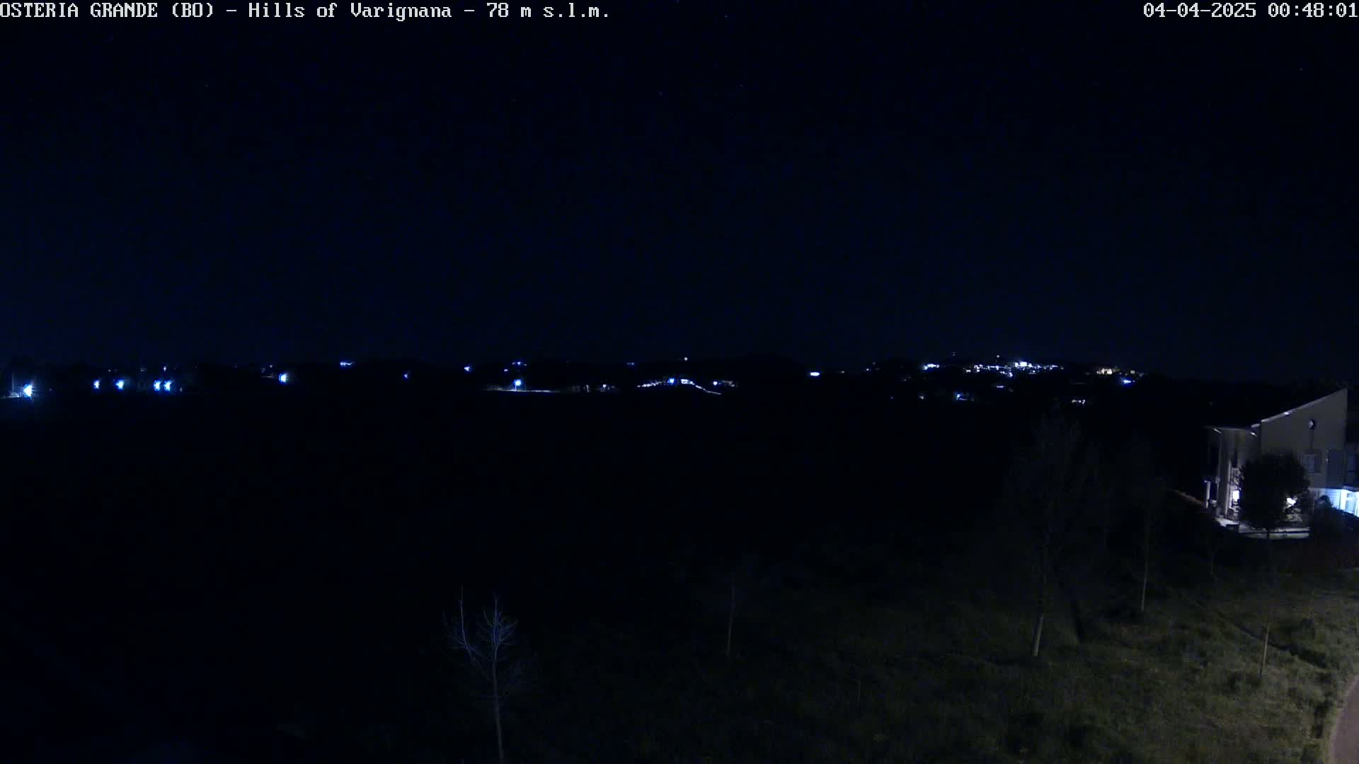 A nighttime view of distant lights in a town or village nestled among dark hills and trees under a clear, dark sky.