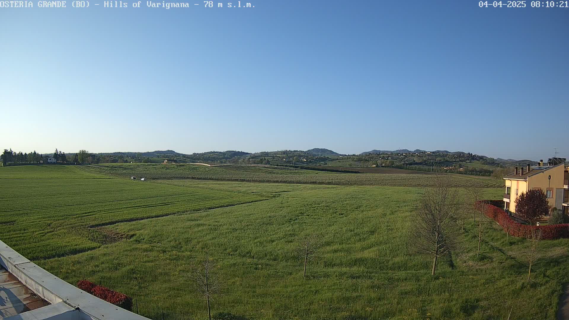 A wide expanse of bright green fields stretches to rolling hills under a clear blue sky.