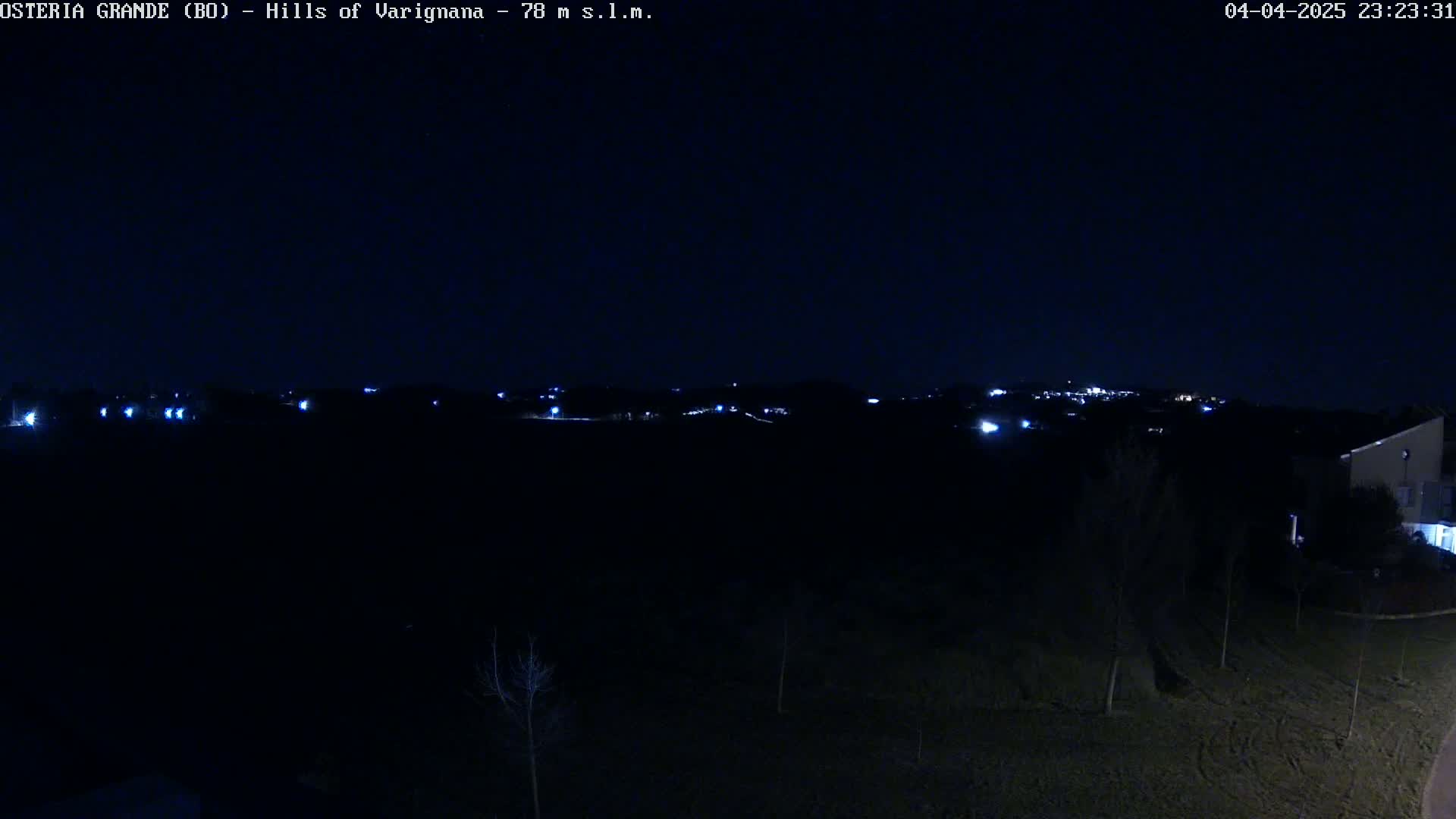A nighttime view of distant lights in a hilly area, under a dark, clear sky.