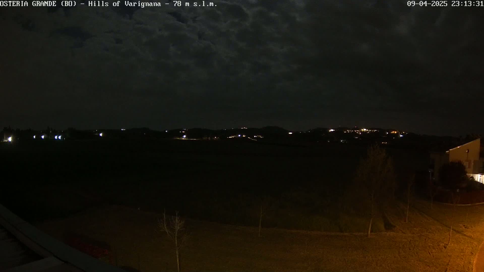A nighttime view of dark hills with a few scattered lights, under a cloudy sky.