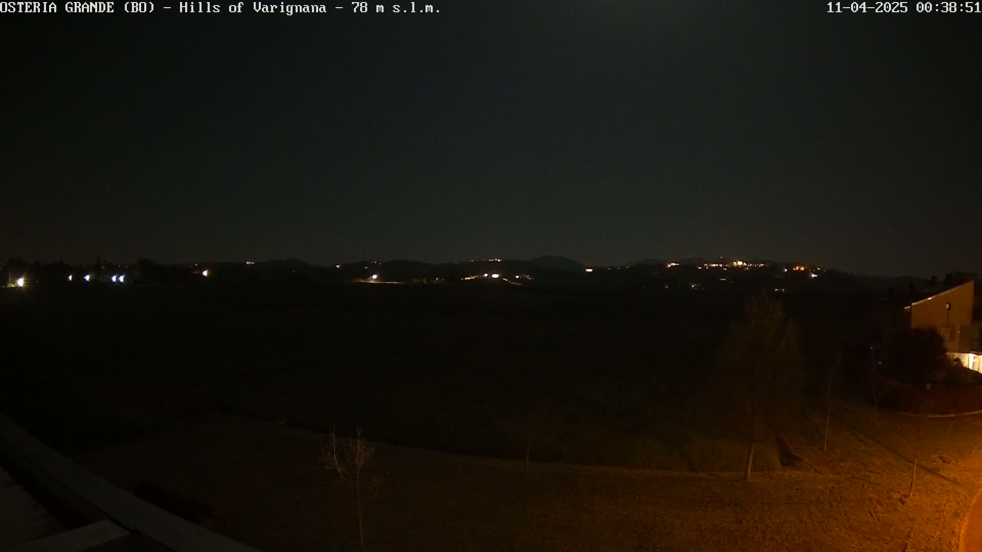 A nighttime view of dimly lit hills and a dark landscape, with a few scattered lights visible in the distance.