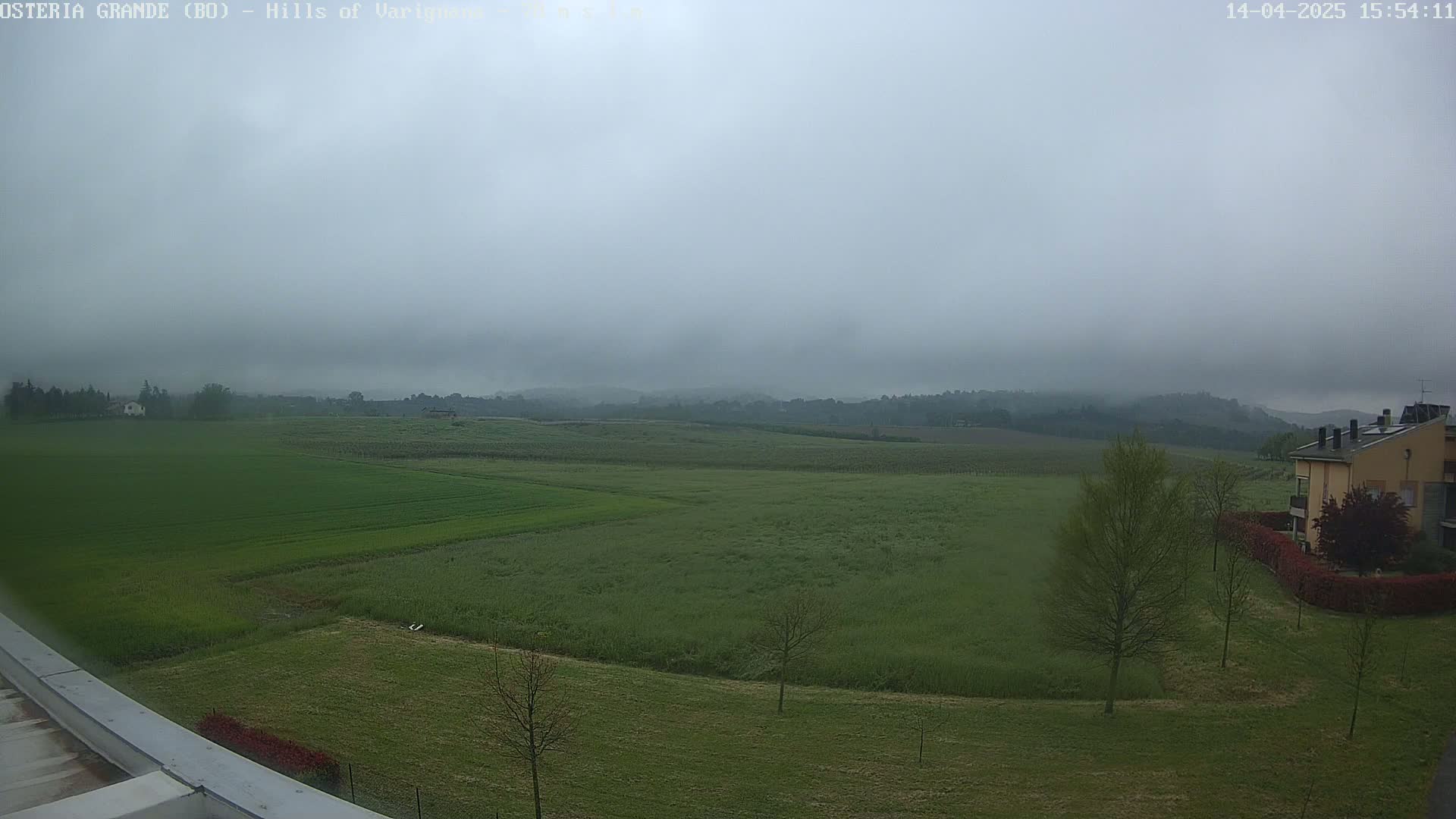 A hazy, overcast day reveals a sprawling landscape of green fields and distant hills, with a few buildings visible in the foreground.