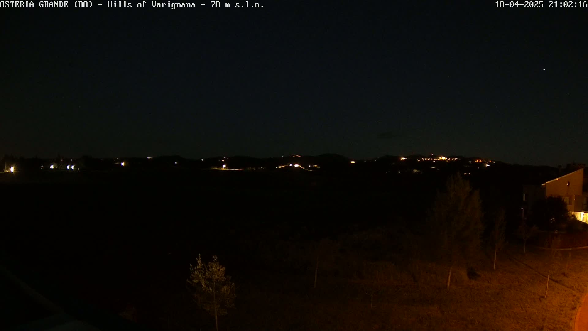 A nighttime view of dimly lit hills and a few buildings, under a clear, dark sky.