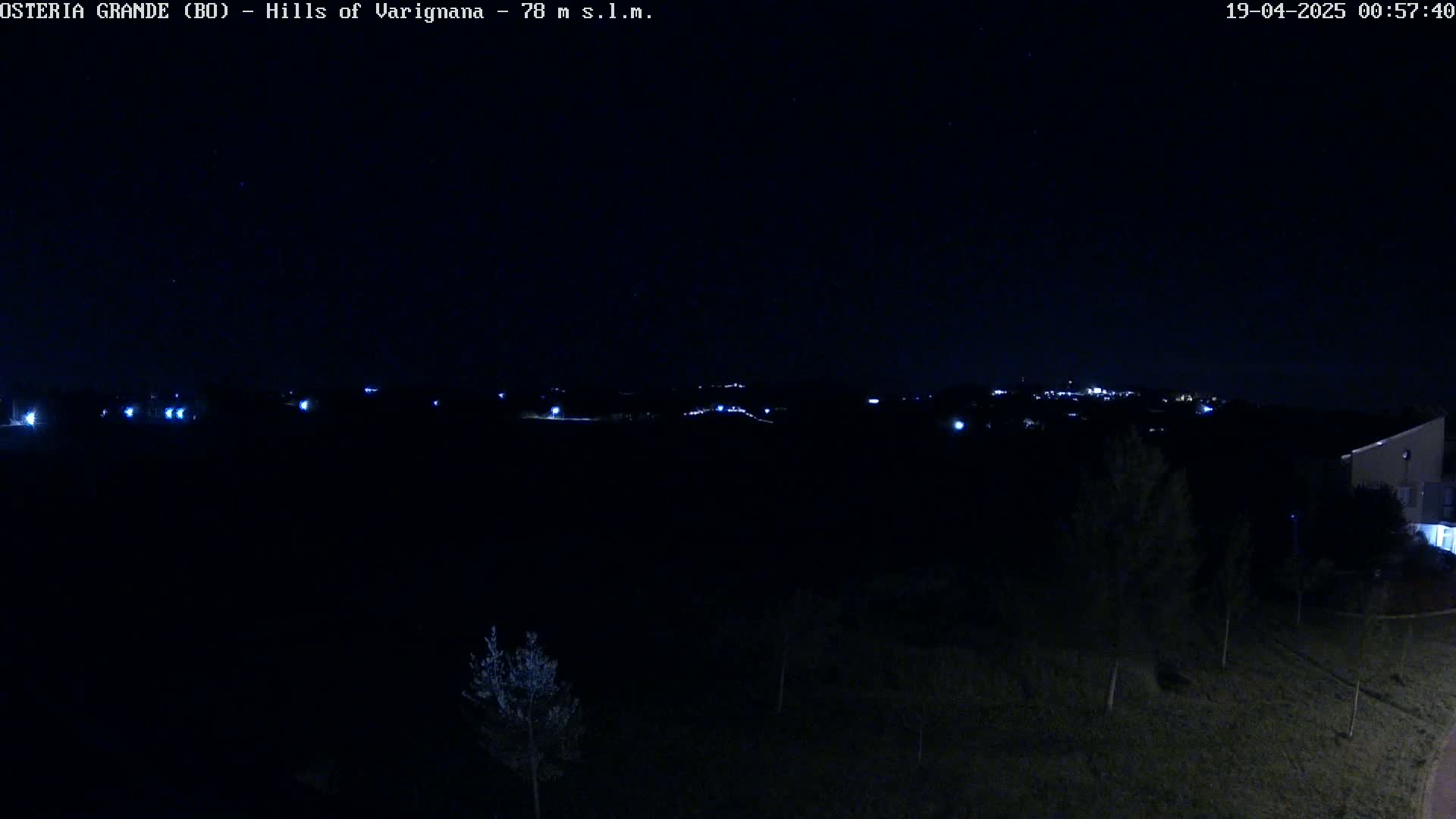 A dark, nighttime view of a landscape shows a few distant lights in the hills under a clear, starlit sky.