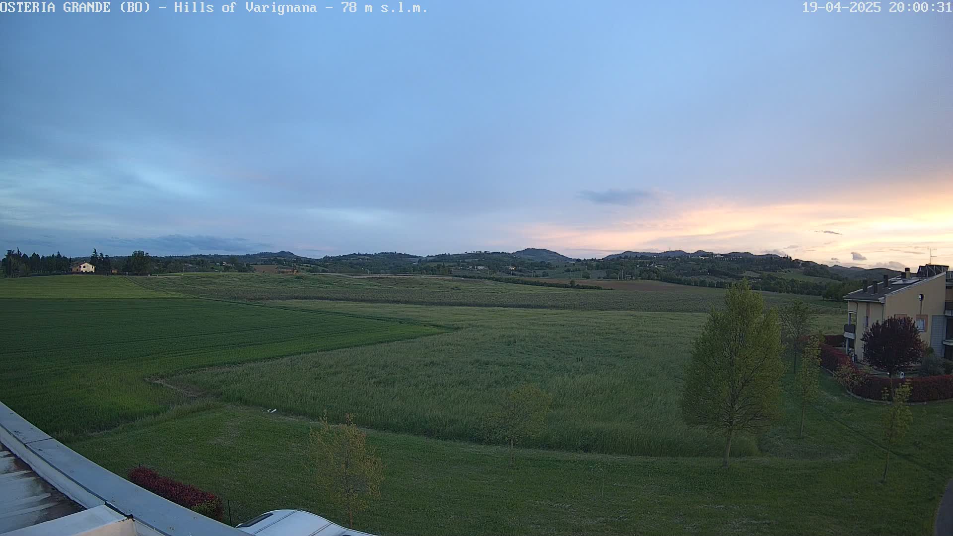 A wide, flat expanse of green fields and low hills stretches to the horizon under a twilight sky.