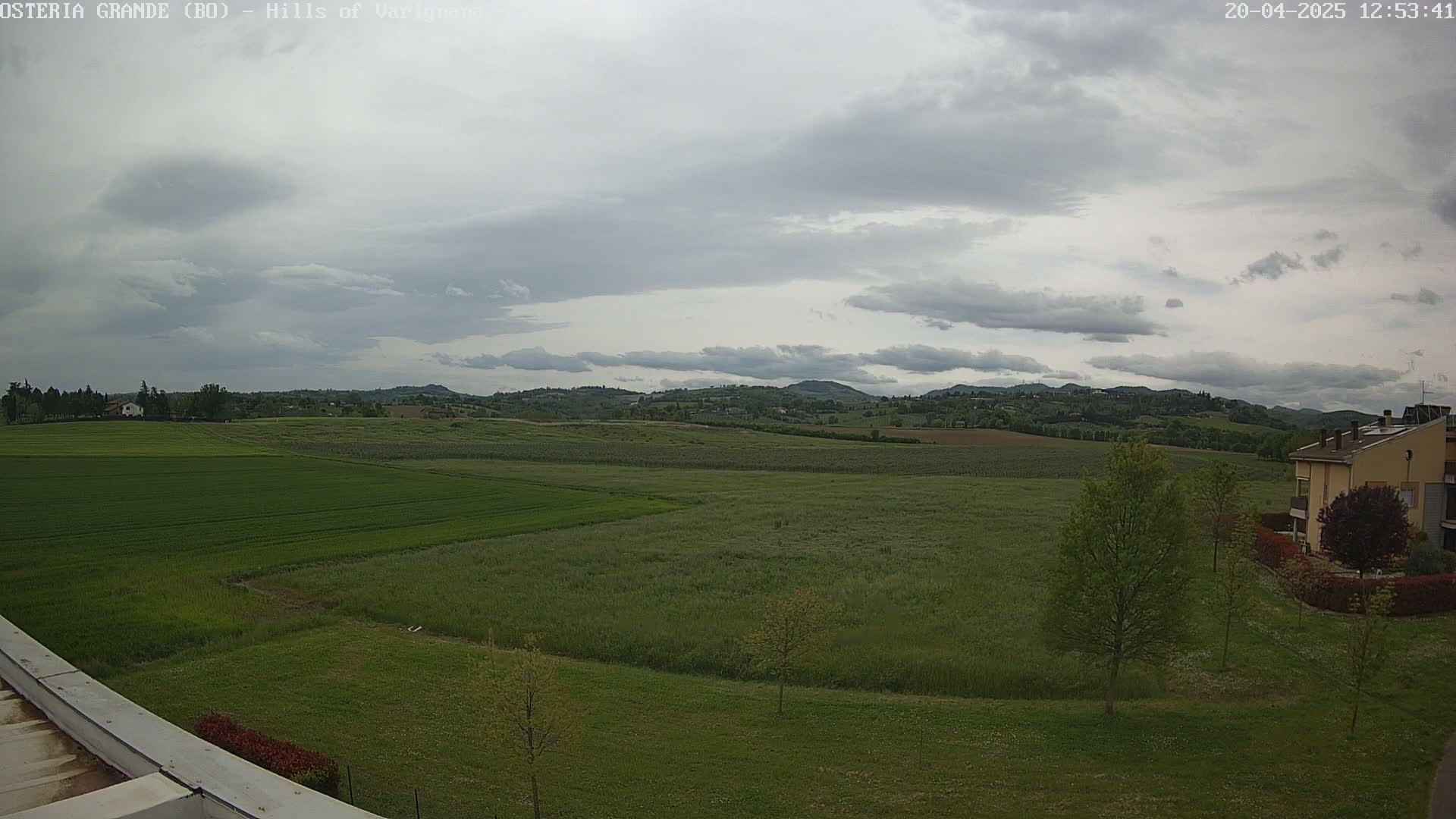 A wide, flat expanse of green fields stretches towards rolling hills under a mostly cloudy sky.