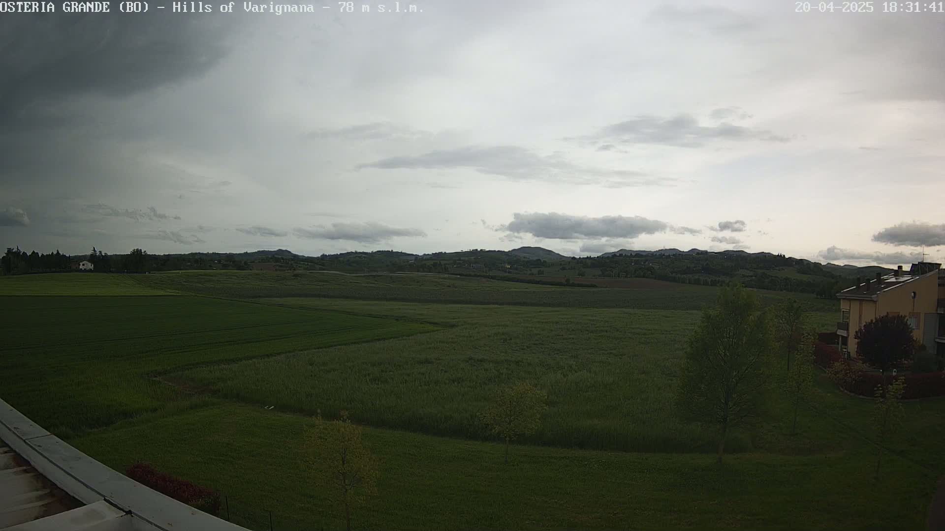A wide, overcast view shows a flat expanse of green fields and distant rolling hills under a cloudy sky.