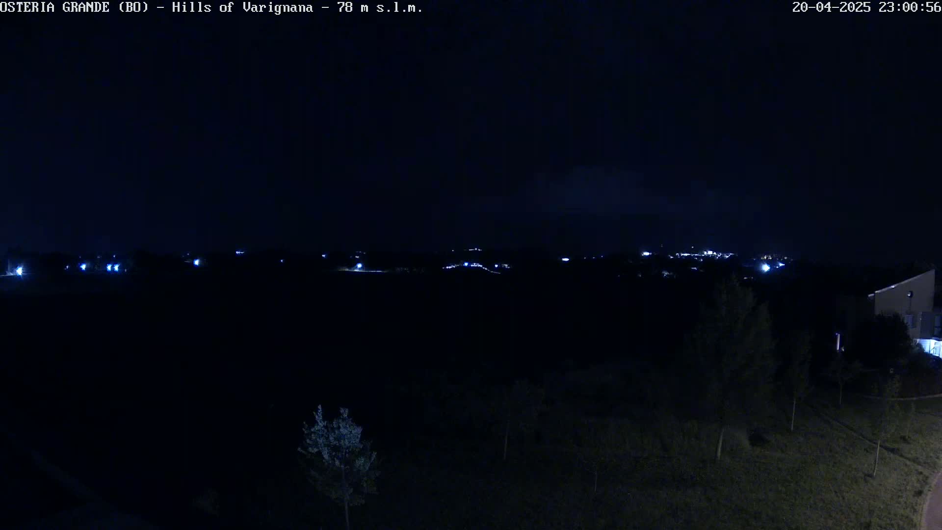 A nighttime view of dimly lit hills and a few buildings under a dark sky.