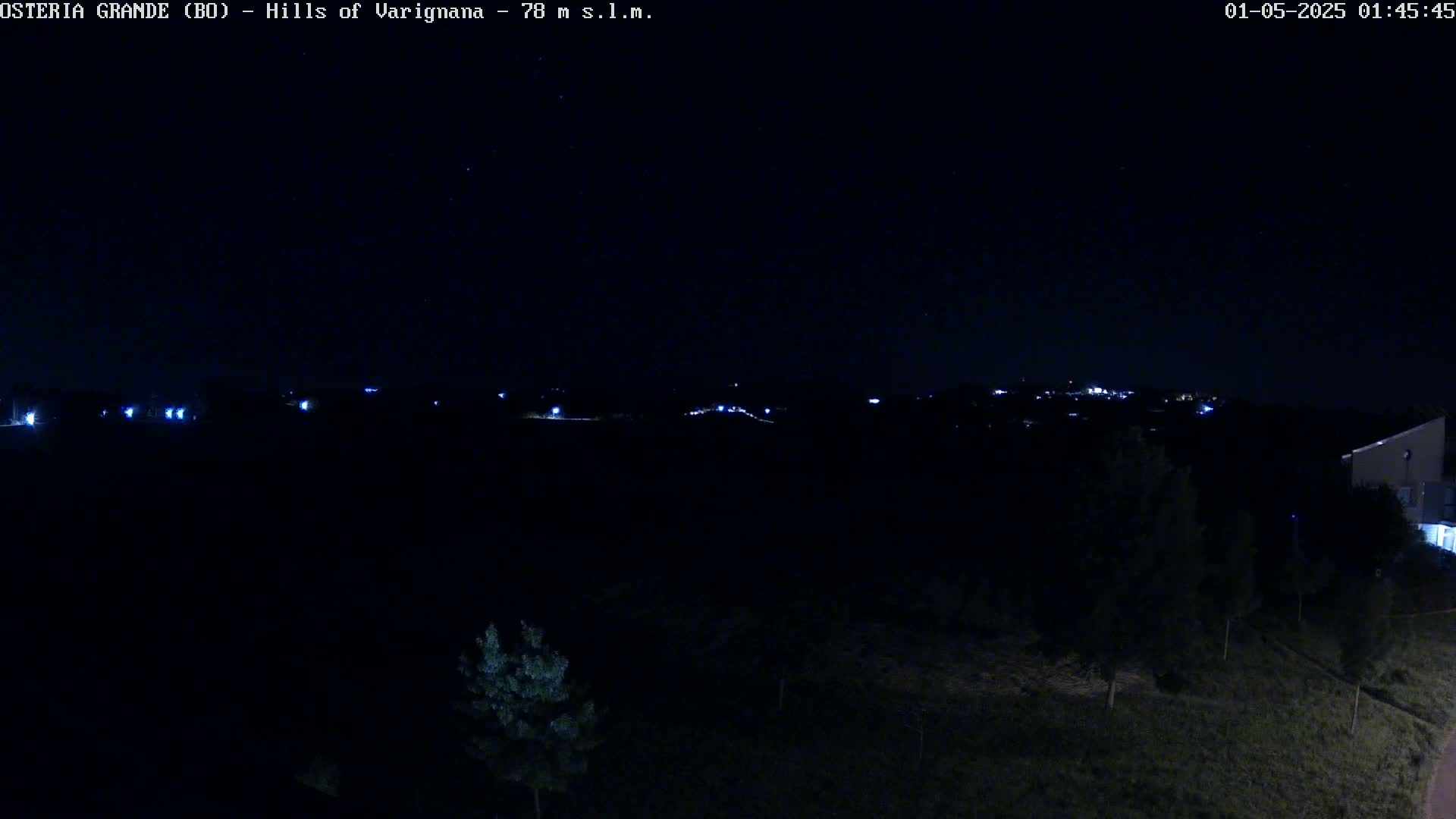 A nighttime view of dark hills with sparsely lit buildings in the distance under a clear, starry sky.