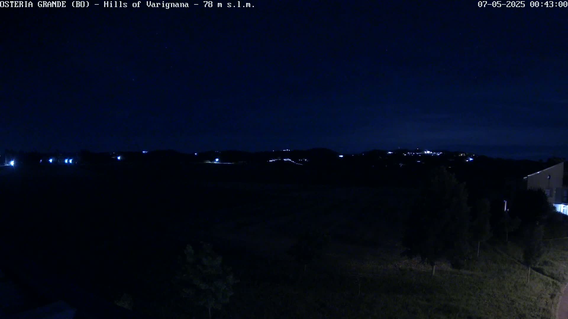 A nighttime view of dimly lit hills and a dark field, under a clear, starlit sky.