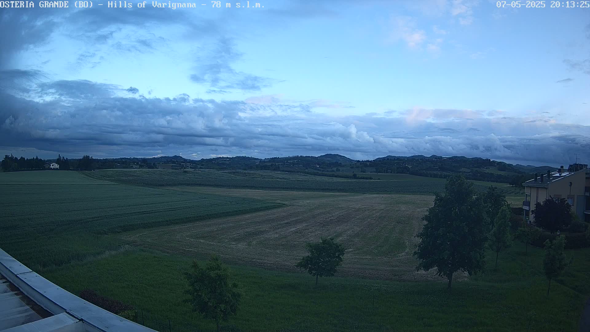 A view of rolling green hills and fields under a partly cloudy twilight sky.