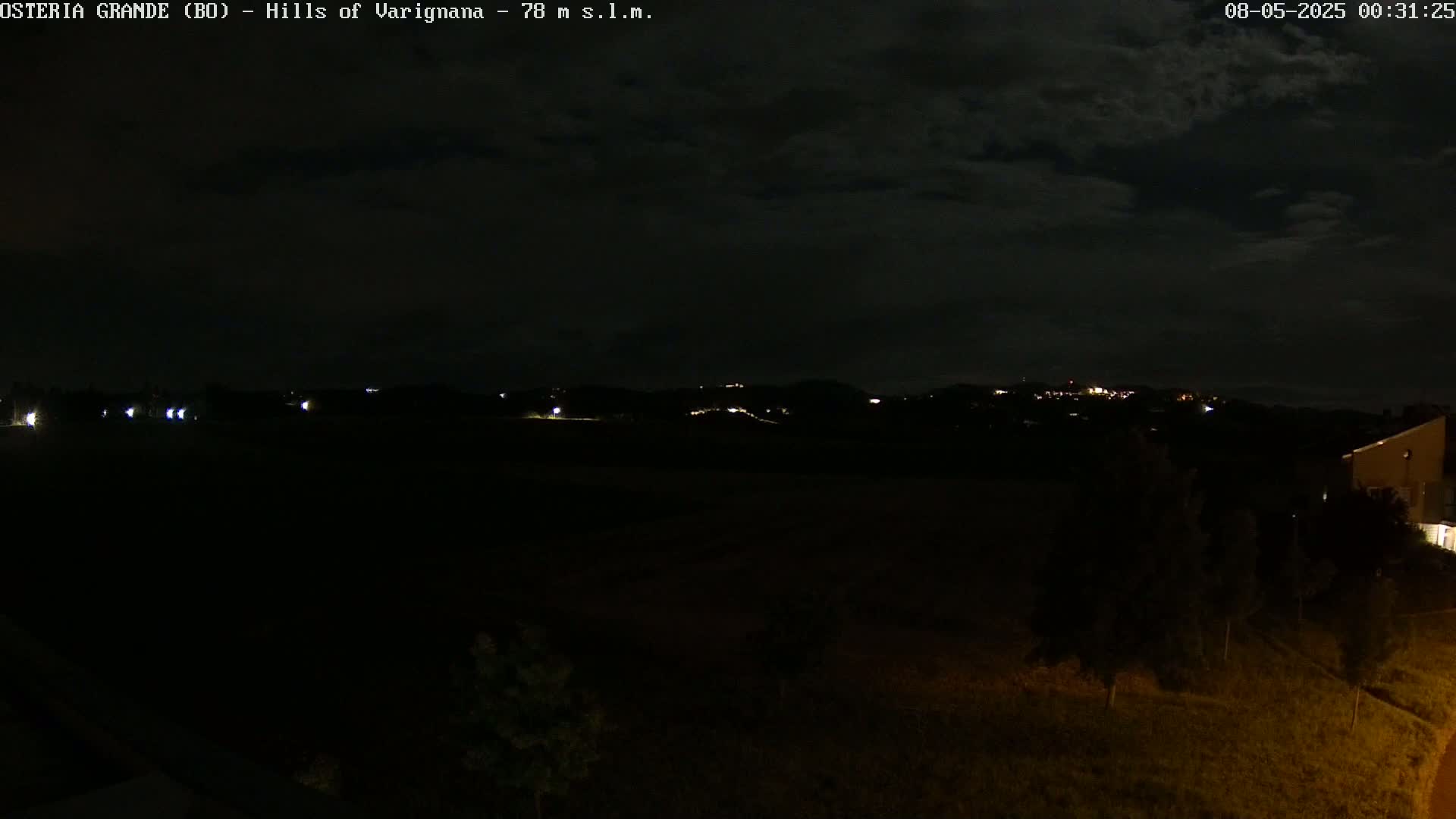 A nighttime view of dark hills with a few distant lights under a cloudy sky.