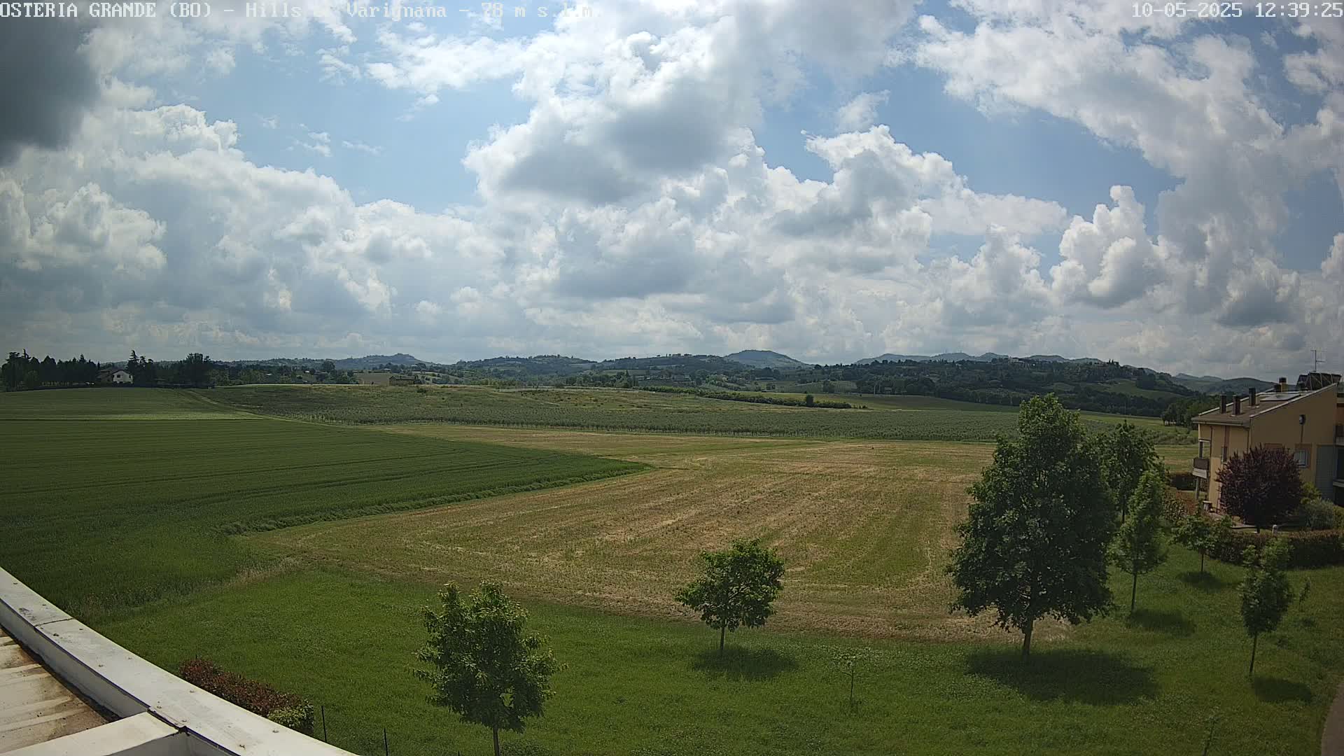 A partly cloudy sky overlooks a vast expanse of farmland, with rolling hills in the distance.