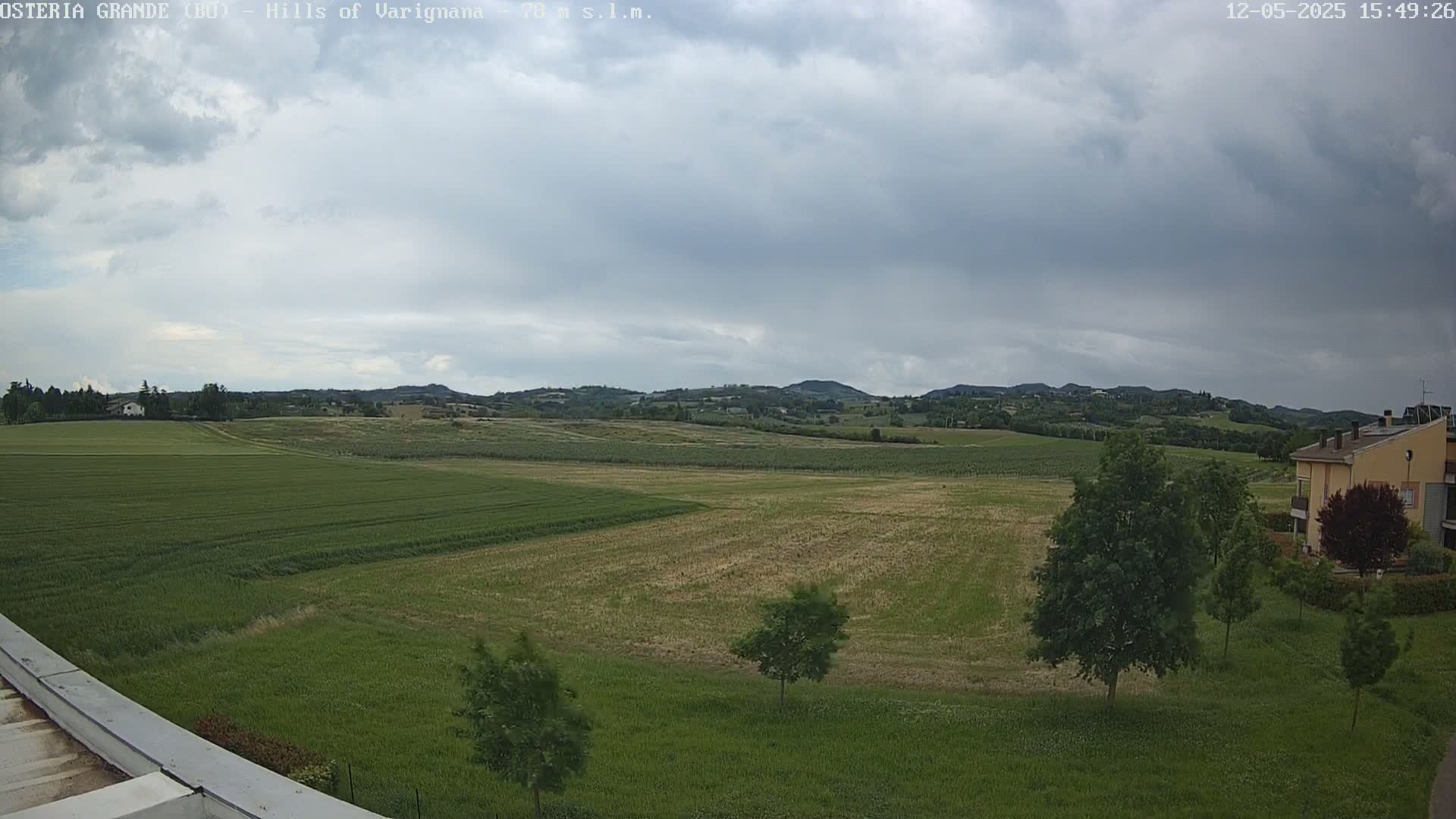 A wide, flat expanse of farmland with varying shades of green and brown under a mostly cloudy sky.
