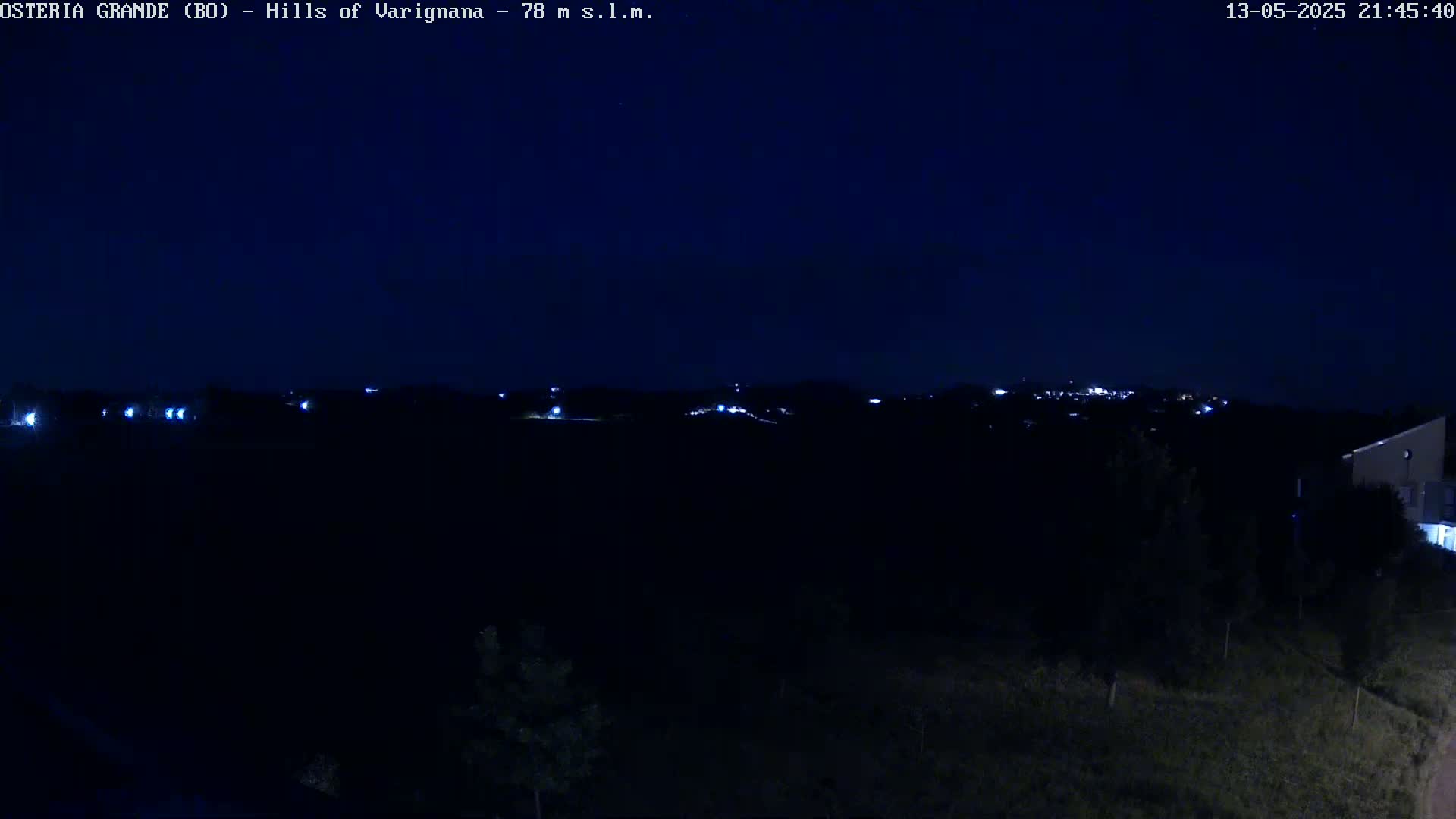 A nighttime view of dimly lit hills and a few distant lights under a dark blue sky.